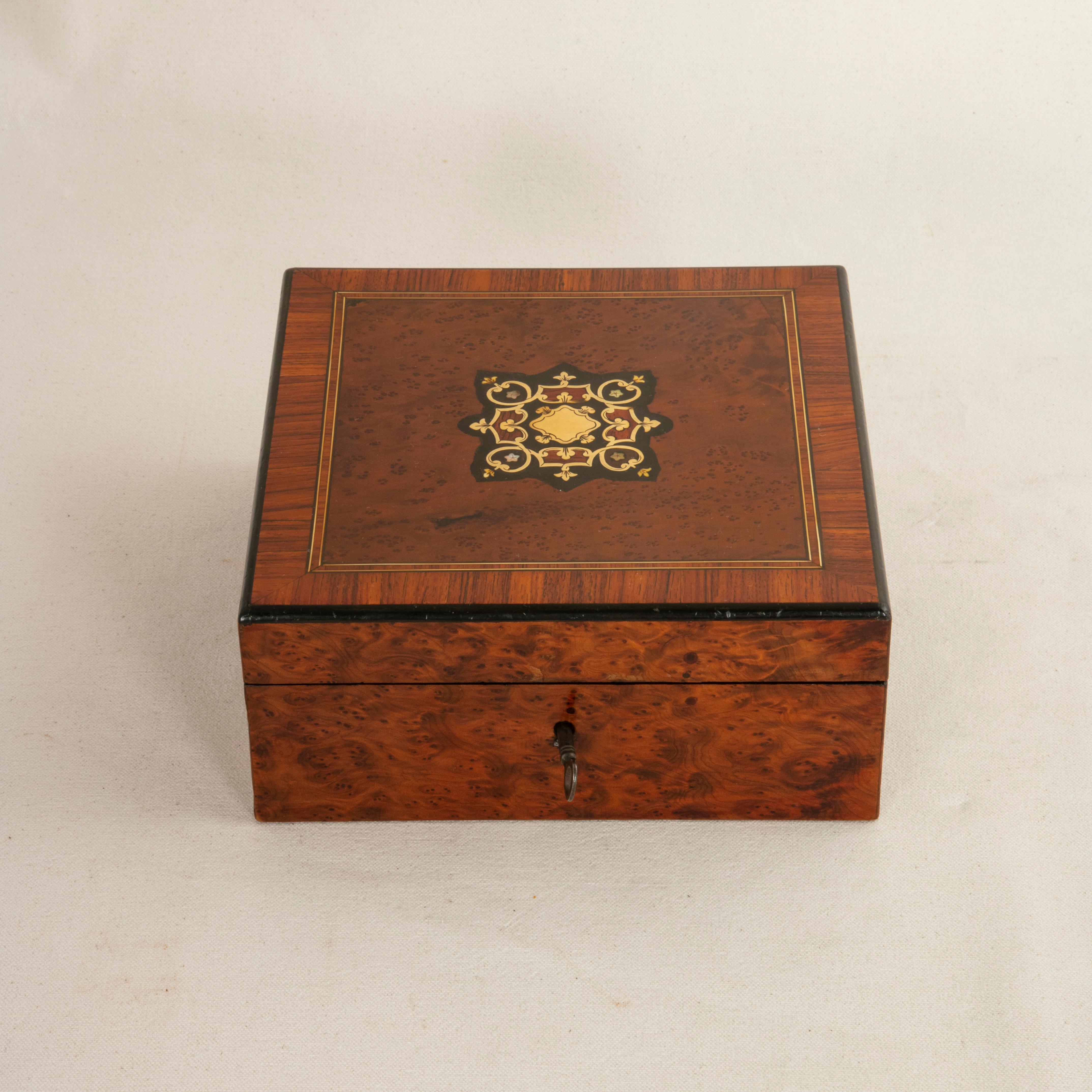 This mid-19th century French Napoleon III period marquetry box features a central field of ebonized pear wood with a bronze cartouche and scrolling bronze inlay. Mother of pearl flowers also detail the central design. The top is additionally