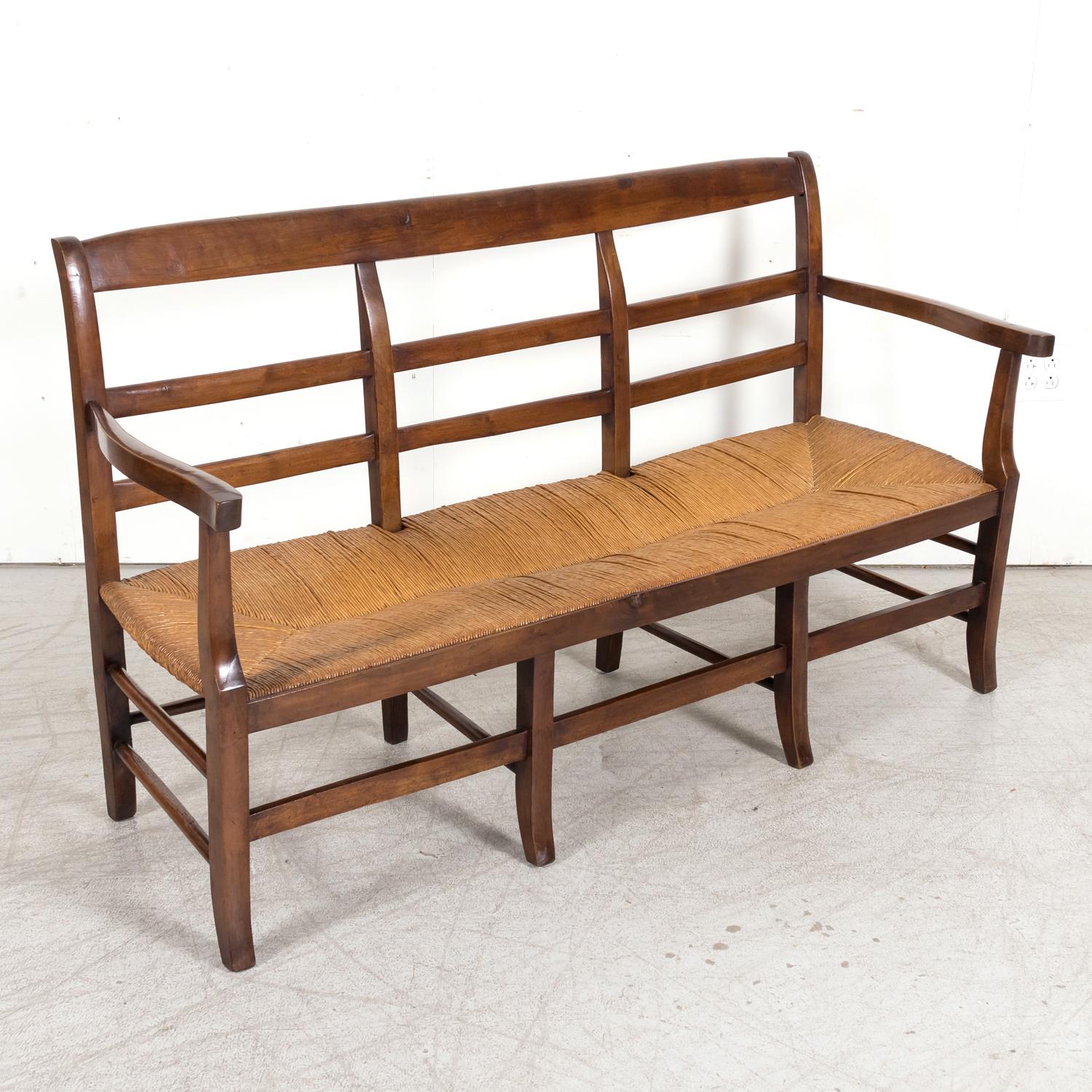 A mid-19th century French radassier or bench handcrafted of solid walnut with a rush seat in Provence, near Avignon, circa 1850s. This double arm Provençal bench seats three and features a ladder-back. A simple yet refined look that captures the