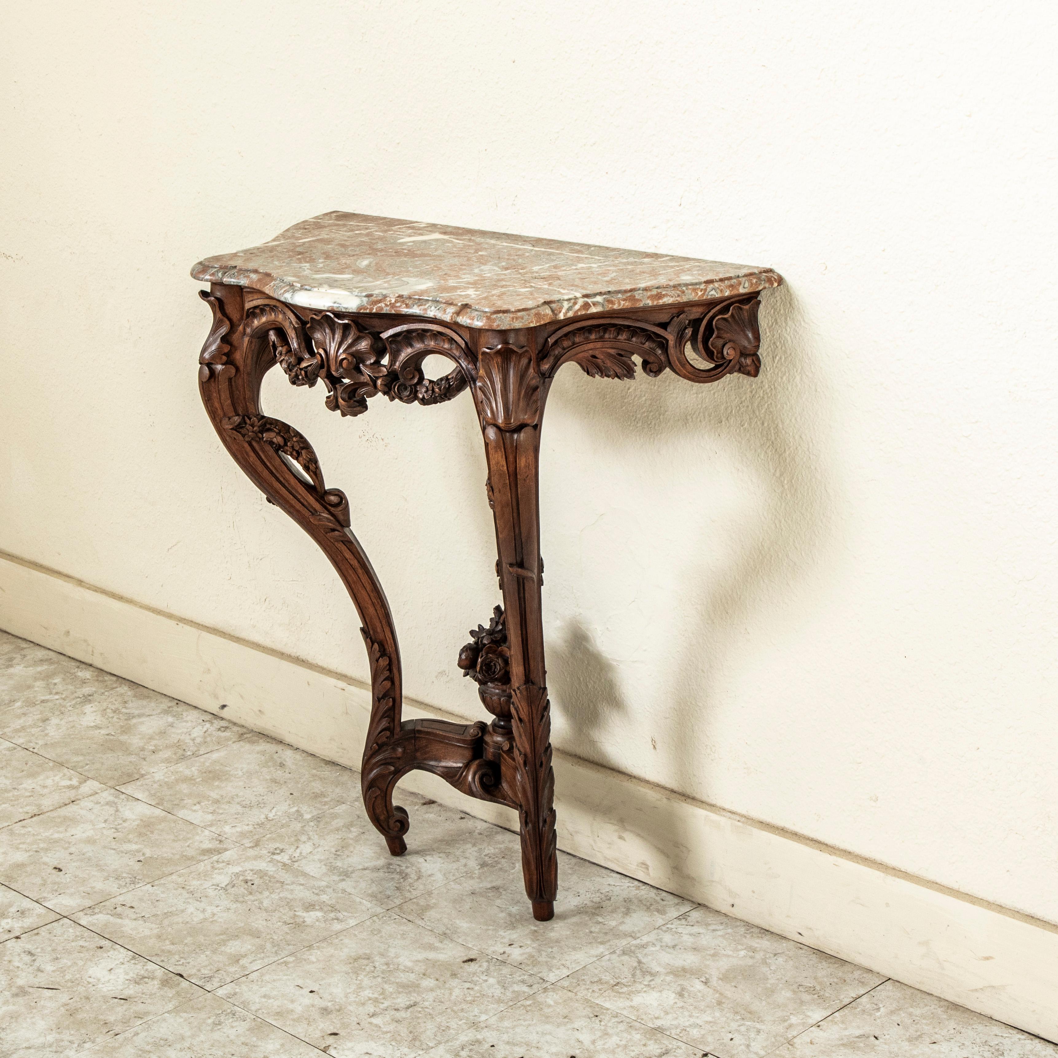 Cette console murale de style Régence française du milieu du XIXe siècle présente un plateau en marbre biseauté et une façade incurvée. Le tablier sculpté à la main sous le marbre est orné d'une coquille festonnée symétrique centrale flanquée de