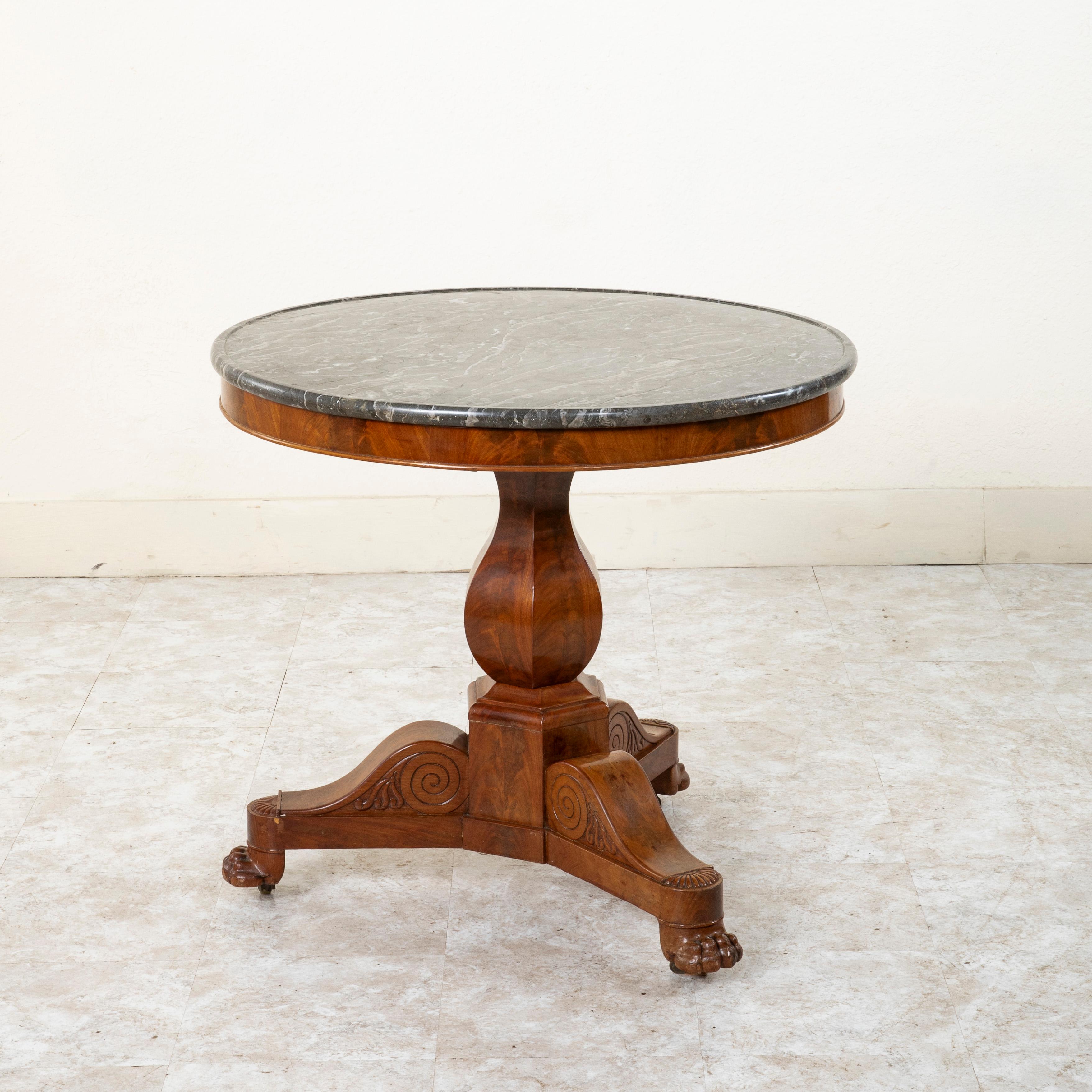 This mid-nineteenth century French Restauration period mahogany gueridon or pedestal table features a beveled Saint Anne marble top. Its 32 inch diameter top is supported by a faceted central pillar that rests on a tripod base. Its three legs are