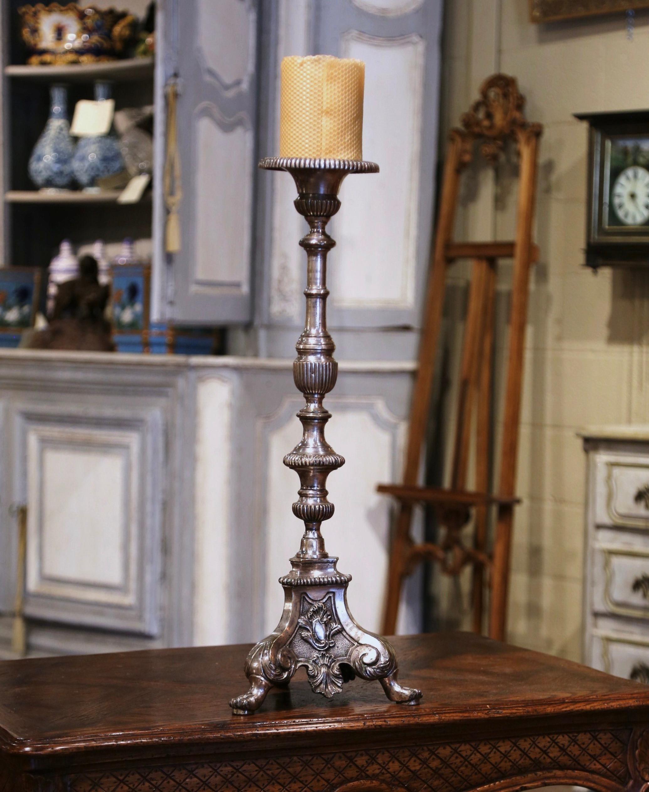 Created in France circa 1860, the elegant antique bronze candlestick stands on paw feet over a triangle base decorated with leaf medallions and shell decor. The tall and heavy candle holder is in excellent condition with a rich patinated silvered