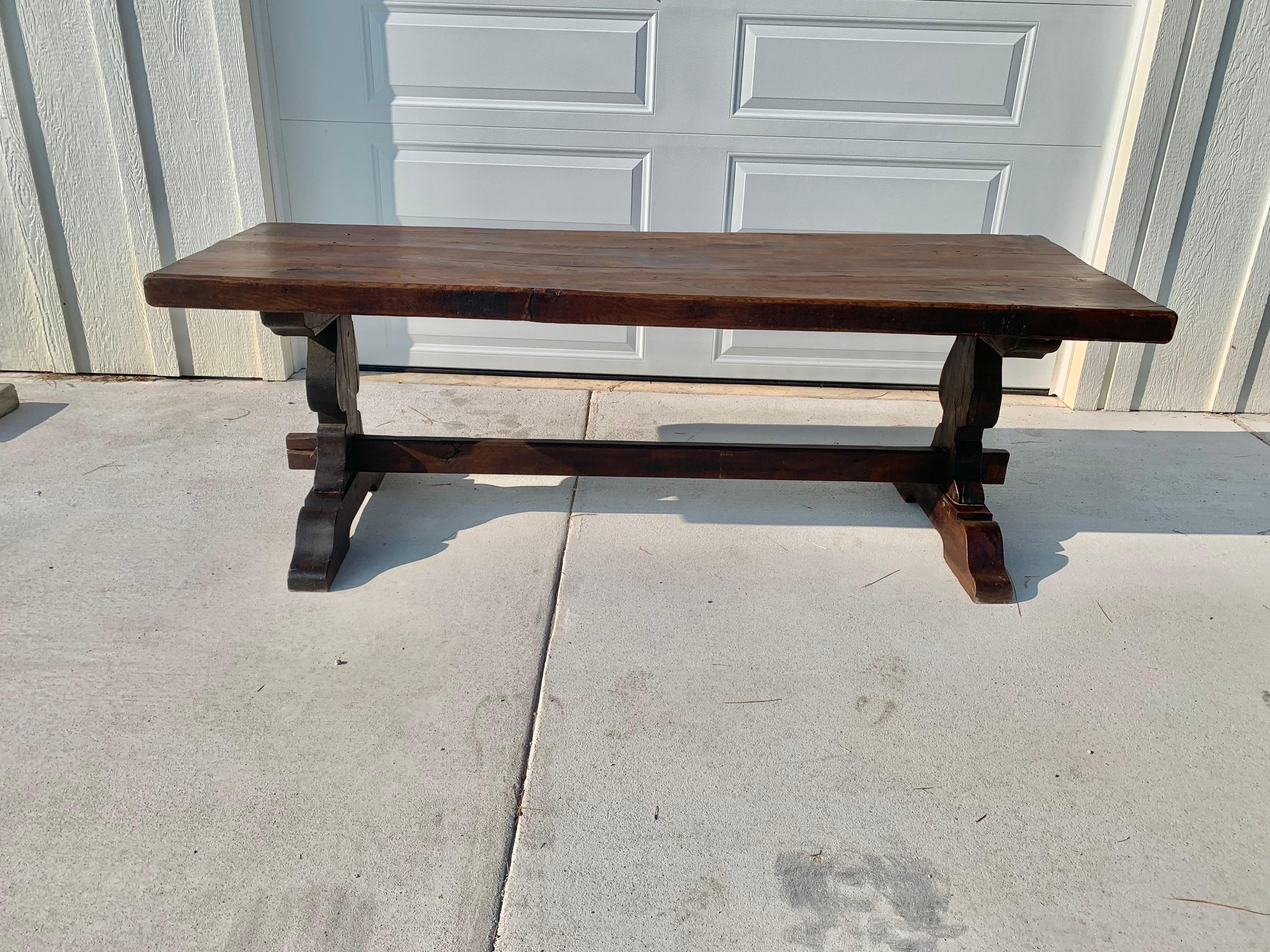Found in the South of France this Mid 1800s French Walnut Monastery Table features a thick wide plank top. The large table is supported by a long trestle style base with hourglass shaped legs ending with wedge pins and wide shoe feet. The hand