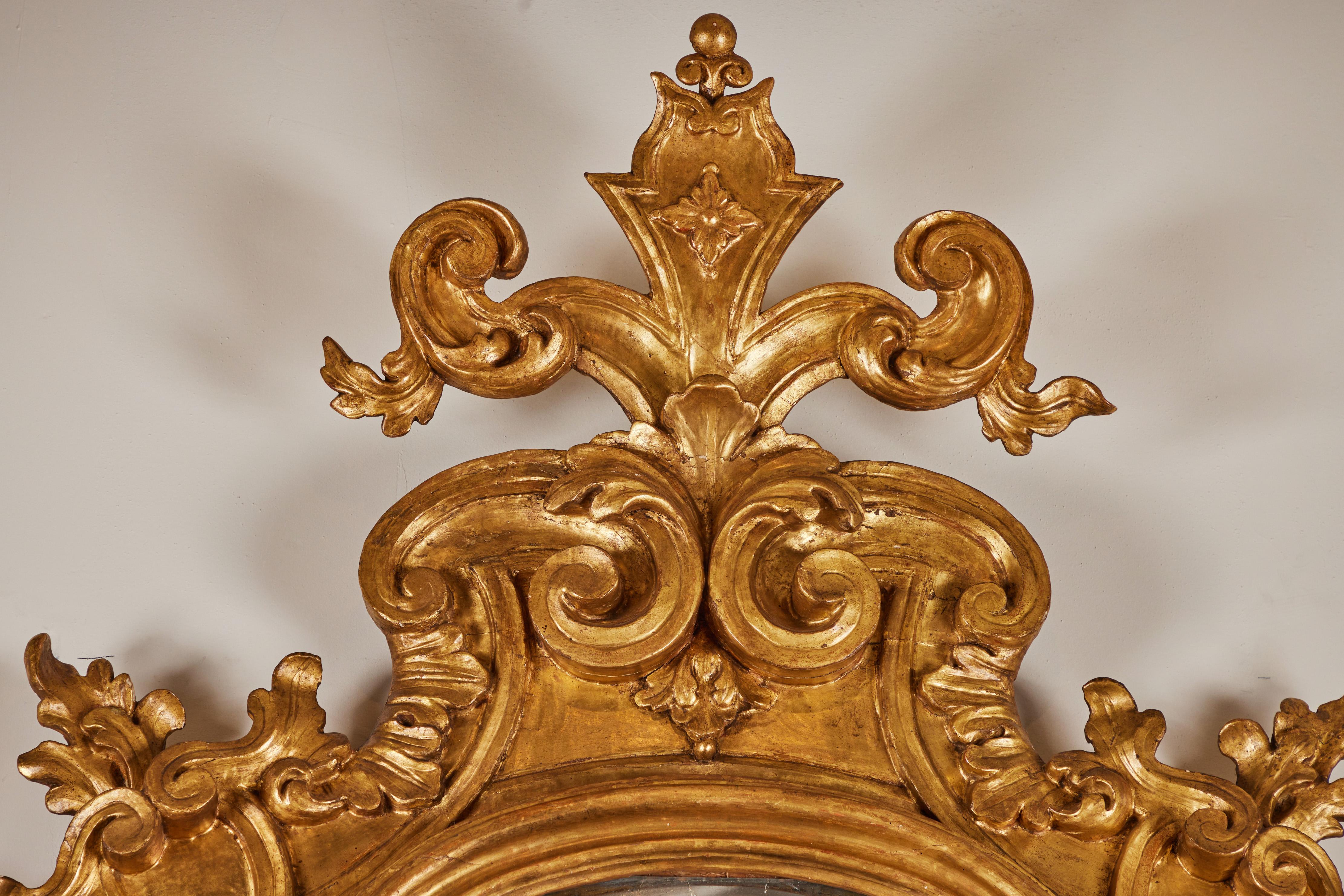 A very large, hand-carved, gessoed and gold gilded, 19th c. mirror with exceptional, foliate carving. The upper extrusions in a broken pediment style, surmounted by a fleur de lis style crown. In the center, on each side, a pair of curling acanthus