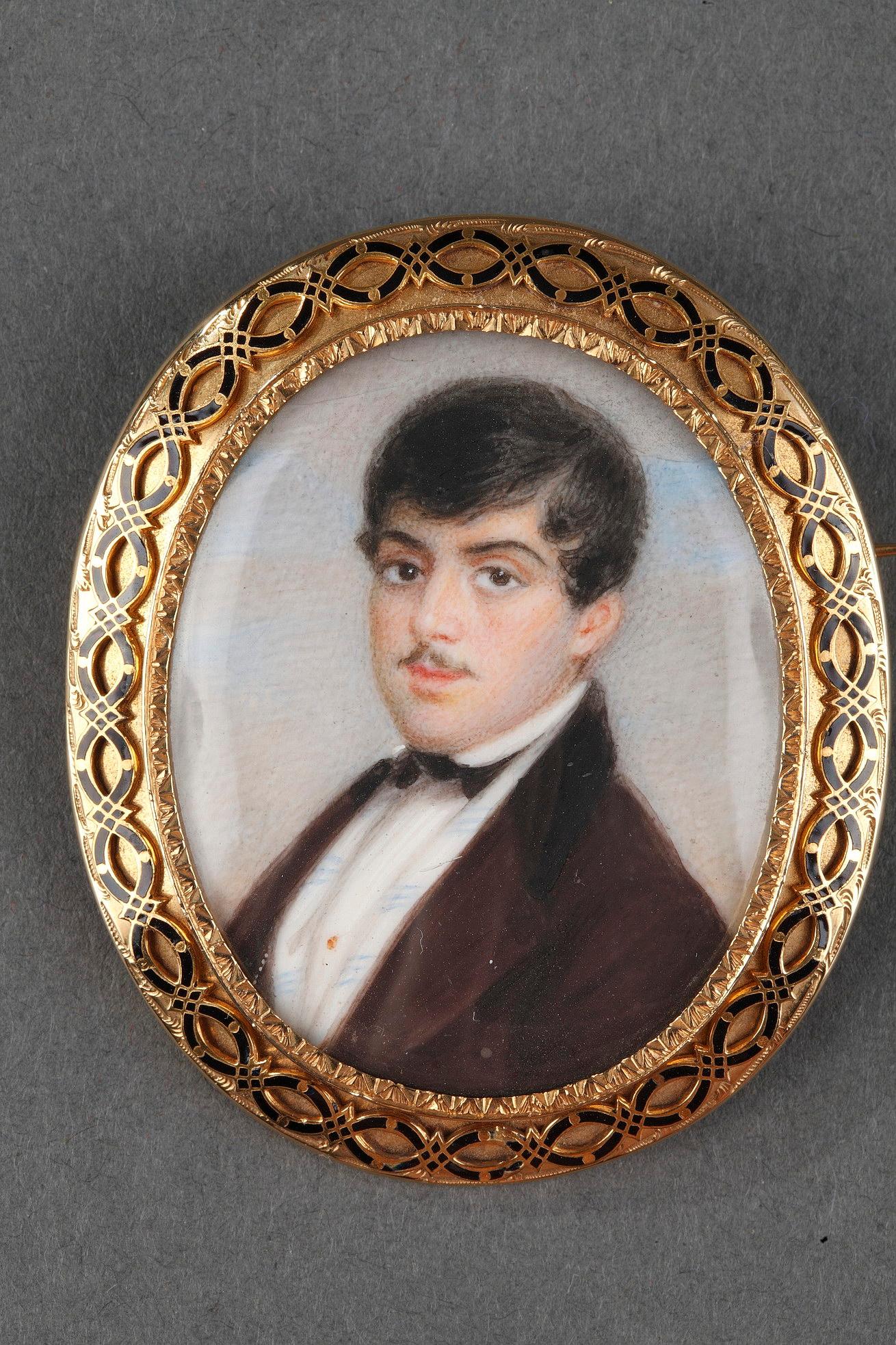 Oval  hand painted miniature mounted in gold enamelled brooch. The frame is in gold and enamelled with fine black enamel threads. The high-quality miniature shows a young man in a brown suit, black collar and bow. The jacket is open over a white