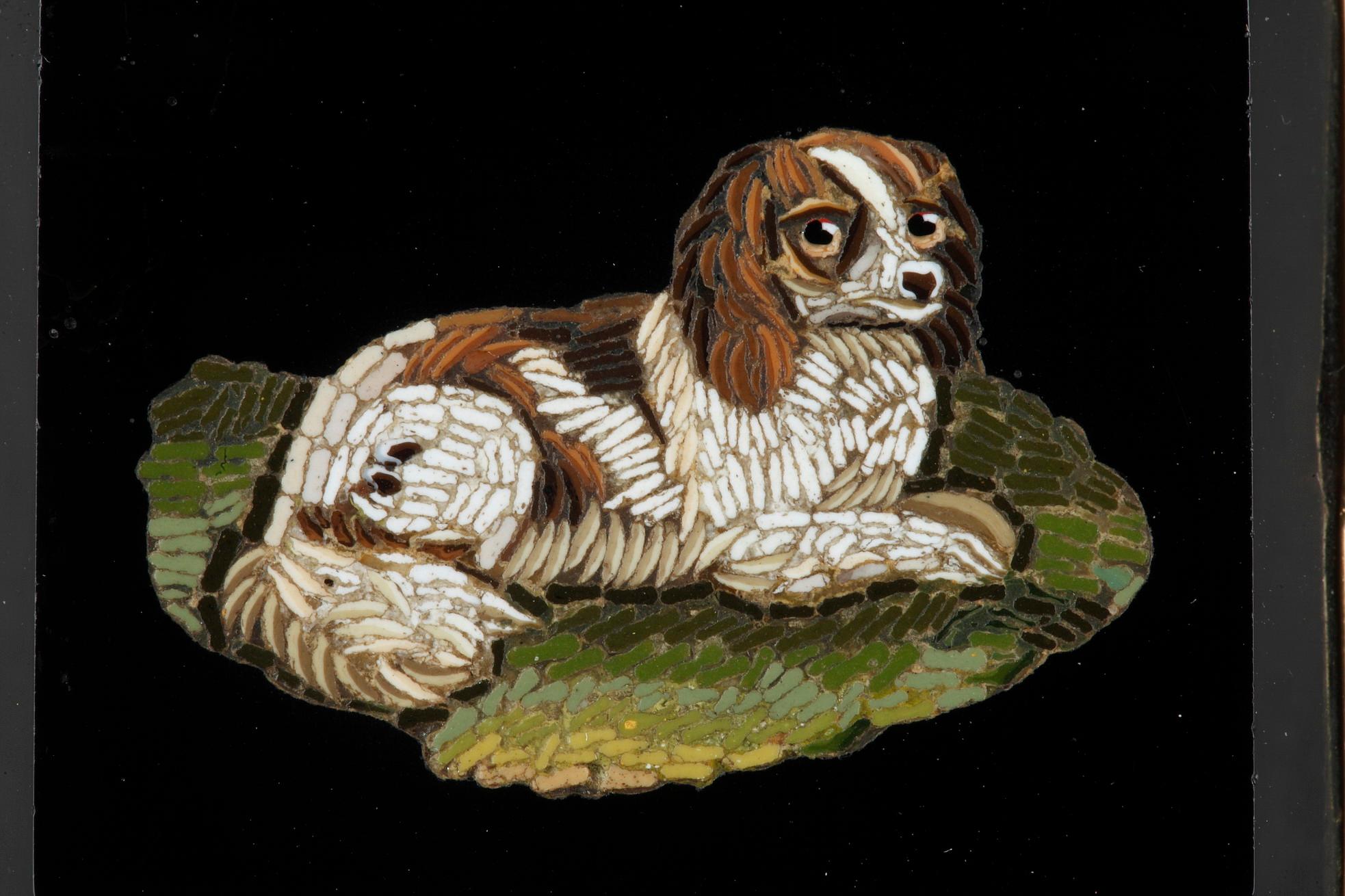 Brooch with a micromosaic set in a gold and royal blue enameled gold setting. Rectangular micromosaic on black onyx representing a spaniel lying in the grass. This composition is by artist Antonio Aguatti. This motif of a dog was a very popular