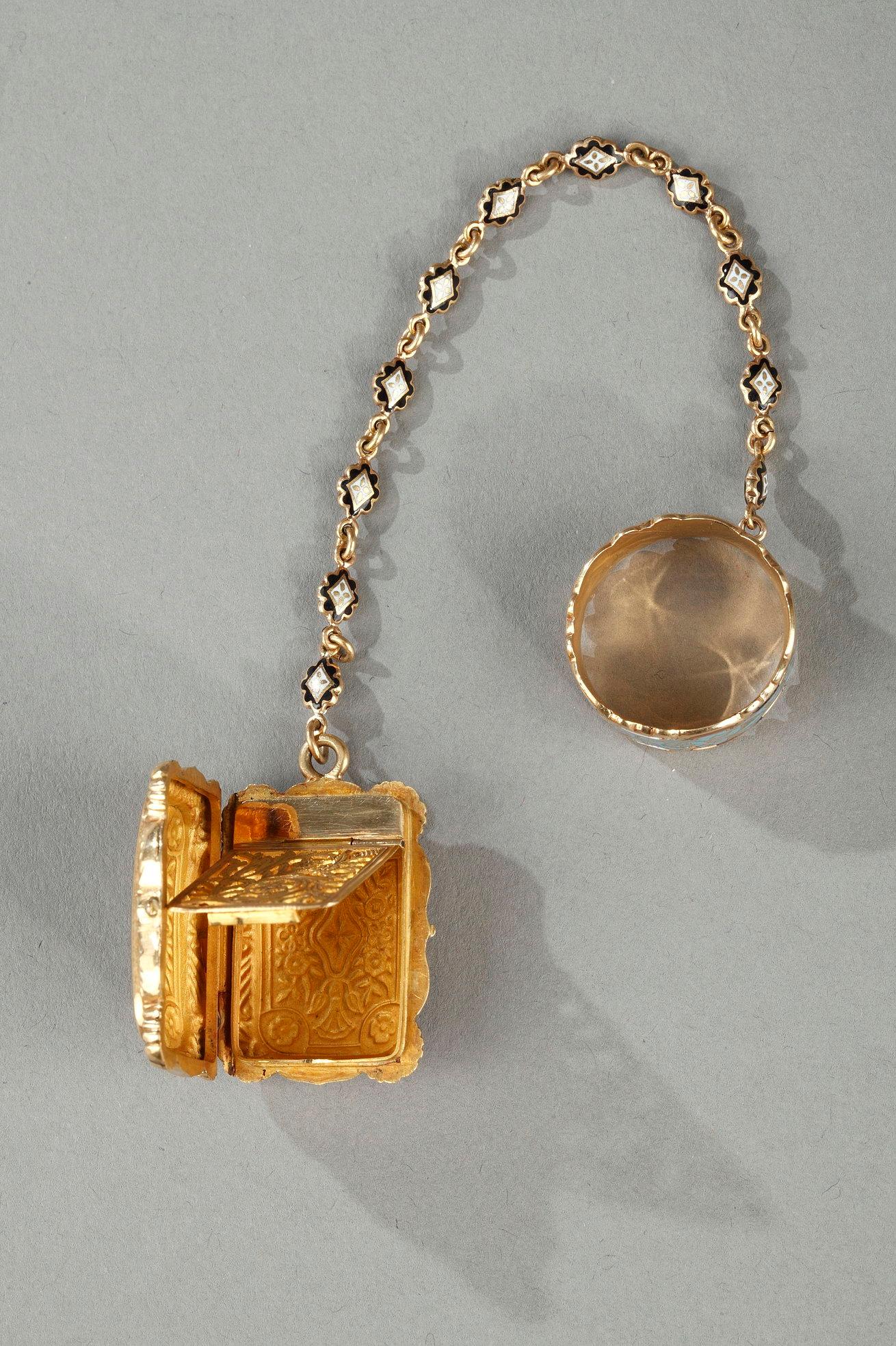 A rectangular vinaigrette in 18-carat gold enameled on both sides with a brightly colored floral composition. A delicate chain connects the vinaigrette to an elegantly enameled ring, highlighted with scrollwork and golden floral motifs. The interior