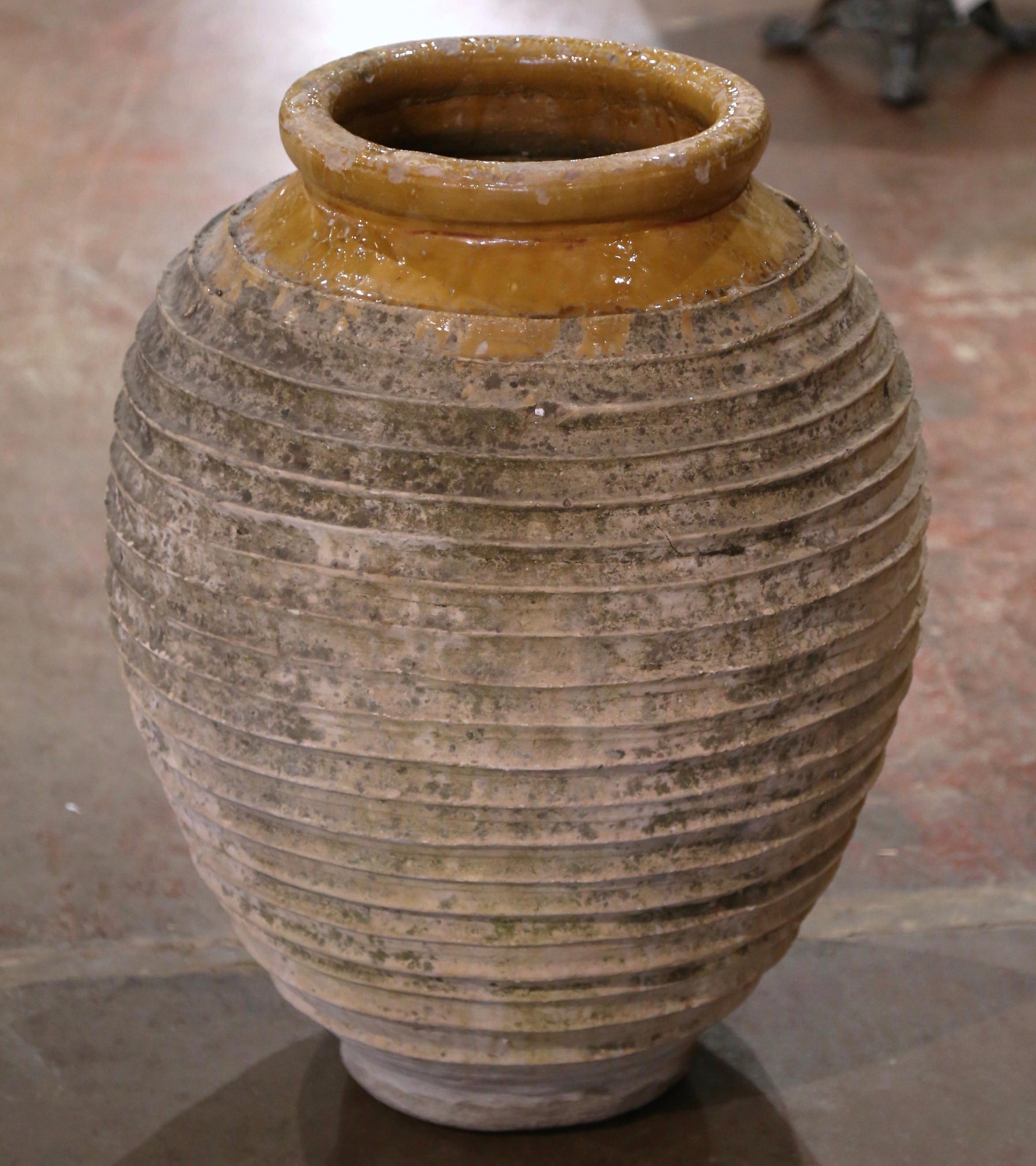 Cette élégante jarre à huile d'olive antique a été fabriquée à la main en Grèce vers 1860.  De forme ronde, avec une base et un col étroits, ce grand récipient présente un bord roulé sur le dessus, accentué par une glaçure couleur moutarde. Le large