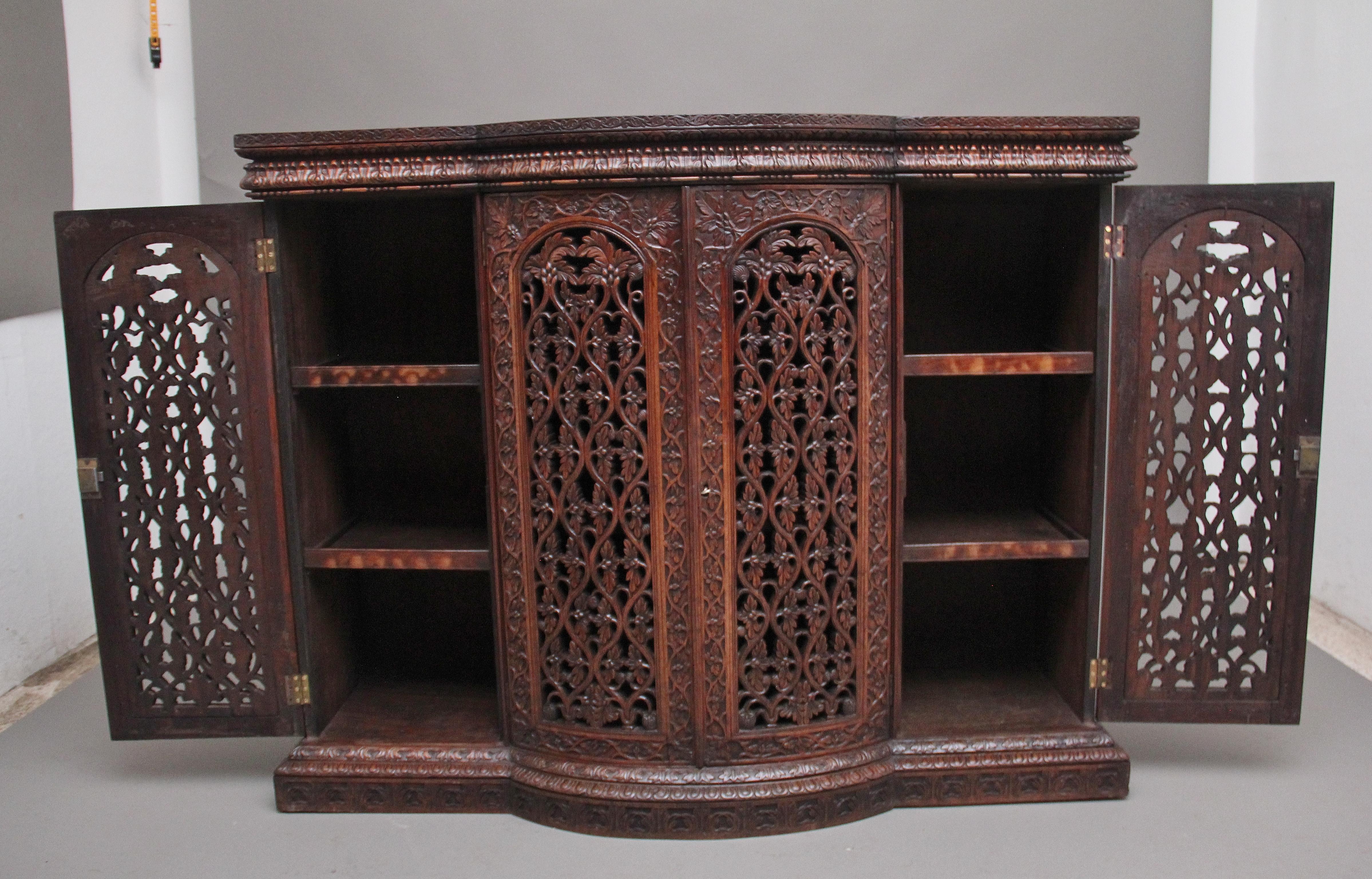 A superb quality 19th century carved Anglo- Indian teak cabinet, the lovely figured shaped top above a shaped frieze with acanthus leaf carving, with four doors below opening to reveal two shelves inside each section, the central doors being bow