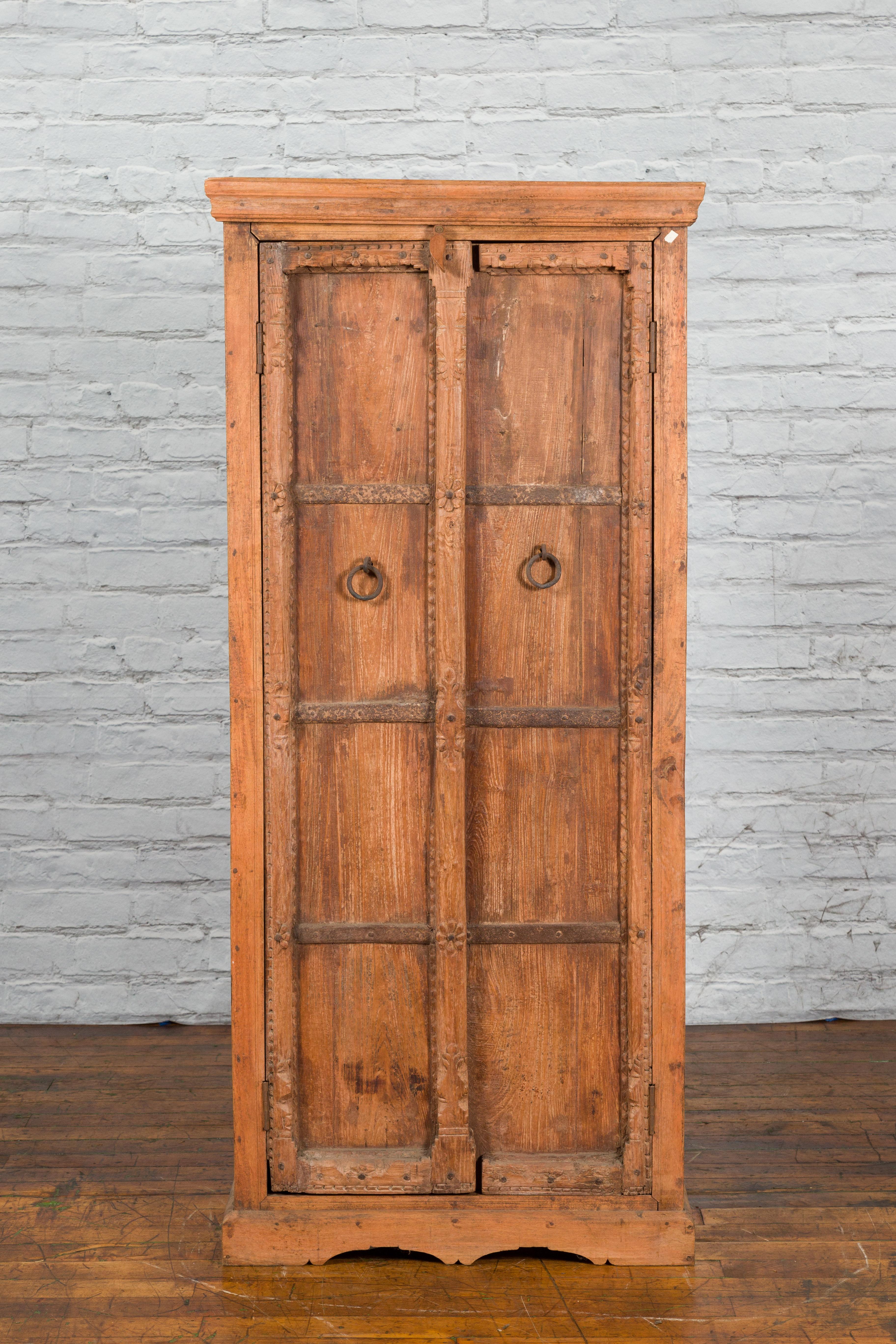 A mid 19th century Indian Gujarat hand-carved wooden cabinet with ring pulls and iron hardware. Created in India during the mid 19th century, this narrow cabinet features a linear silhouette beautifully accented with hand-carved floral motifs and