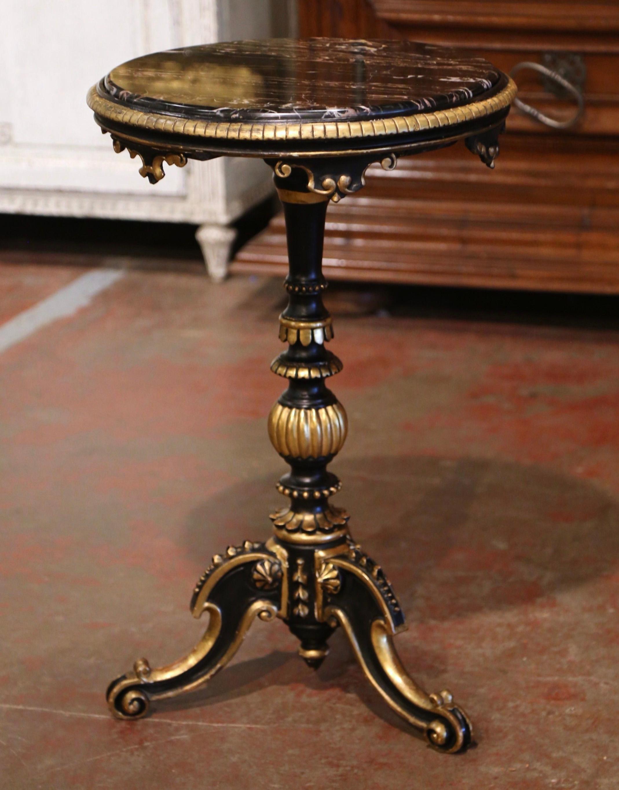 Crafted in Florence, Italy, circa 1860, this elegant antique table stands on a carved and turned pedestal base ending with three legs and escargot feet, decorated with floral gilt motifs. The surface is dressed with a circular inset black marble top