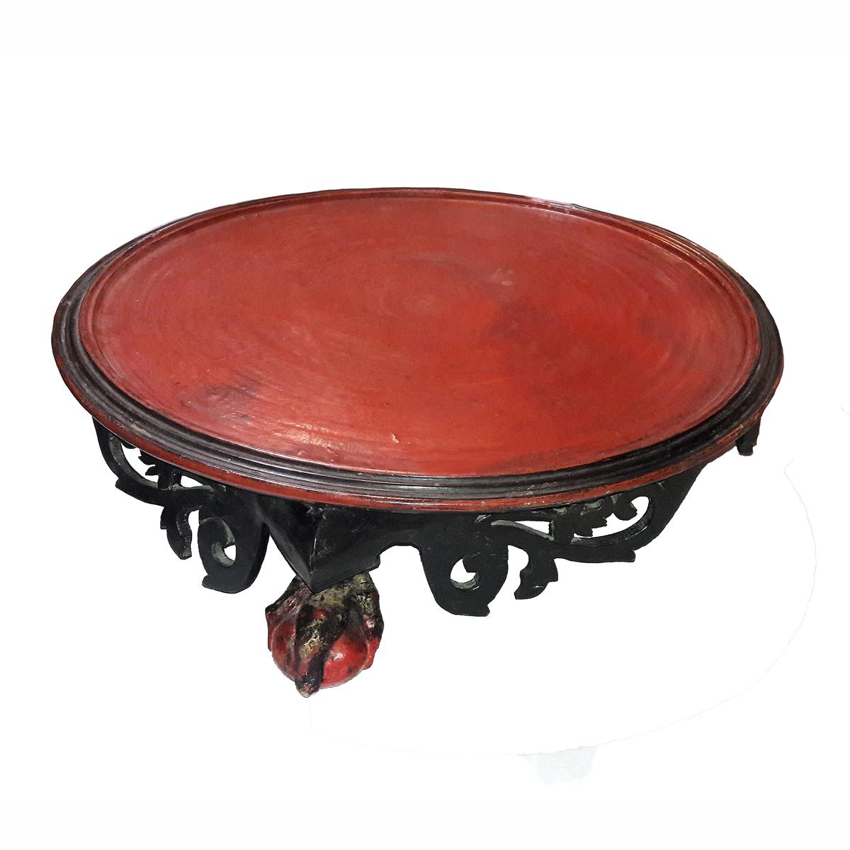 A round wood offering table with red painted top and black ornately carved base with claw and ball feet. Dimensions: 27