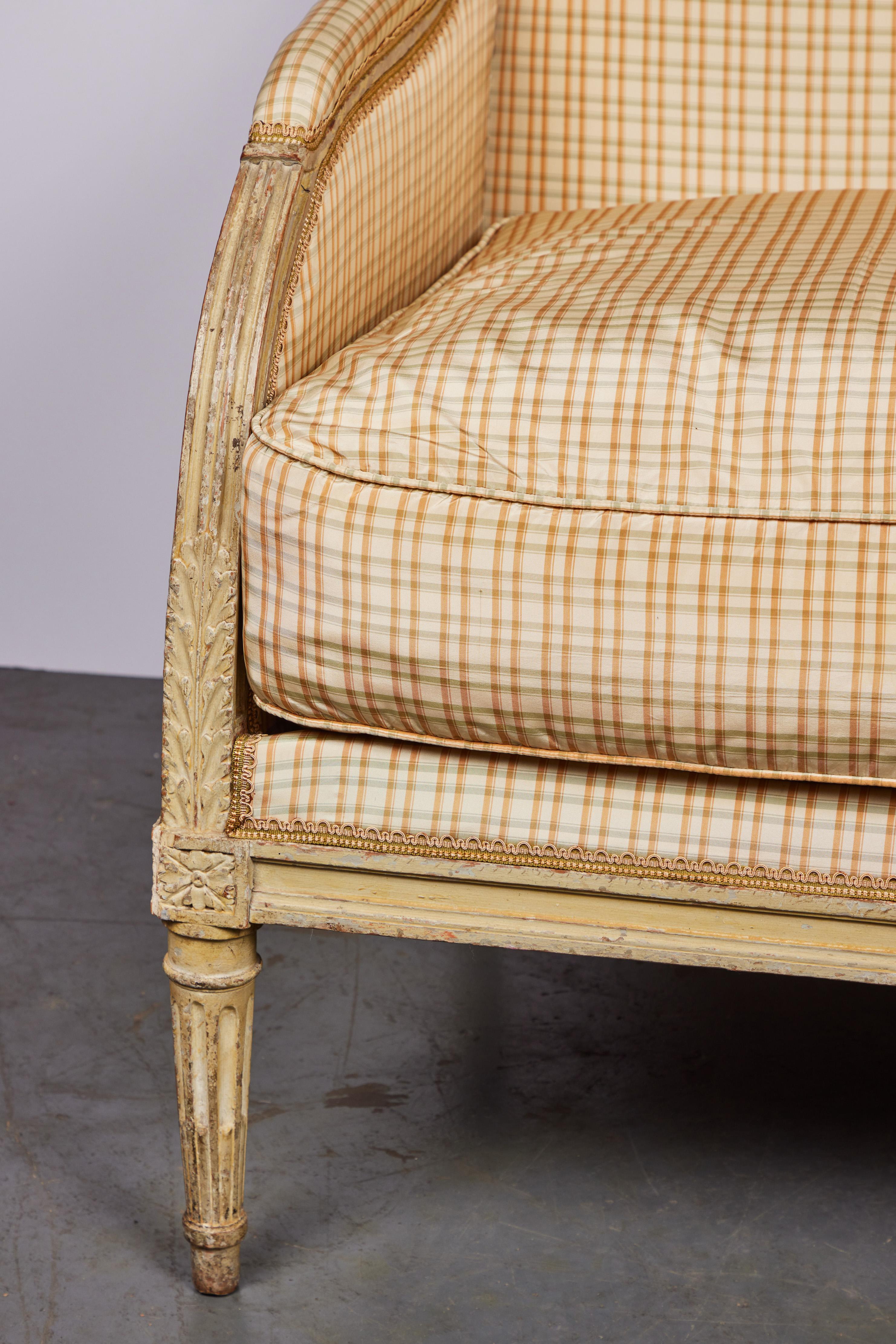 A fine, 19th century, hand-carved marquis chair with paint traces, foliate reliefs, and finished in plaid silk,  trimmed with gimping. The whole in original paint, and sitting on fluted legs.