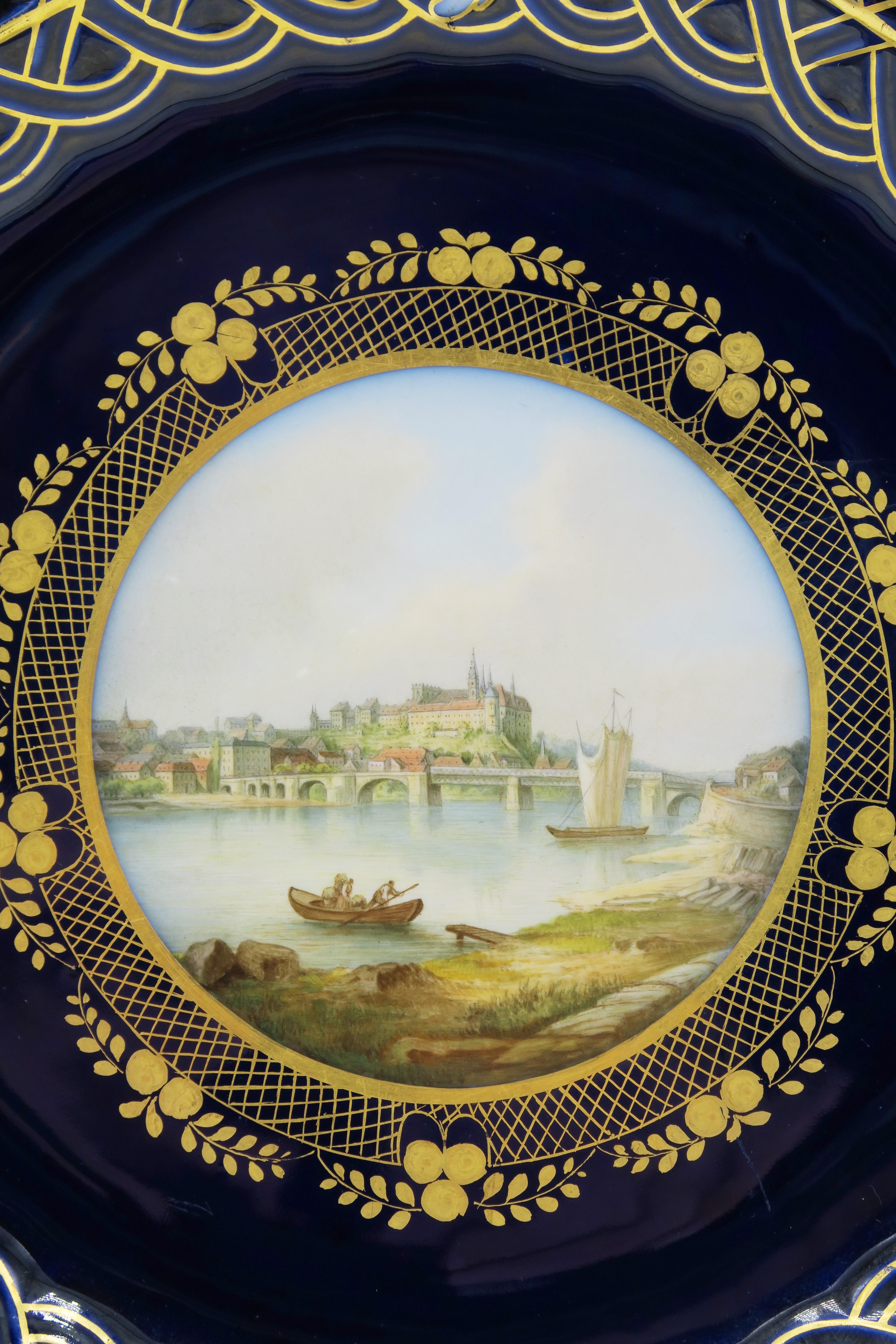 Mid-19th century Meissen landscape dekorative plate

Reticulated porcelain plate with gold rim and cobalt blue background. Three groups of colored flowers are drawn on the edge of the disk. The landscape of Dresden is drawn in the middle. Meissen