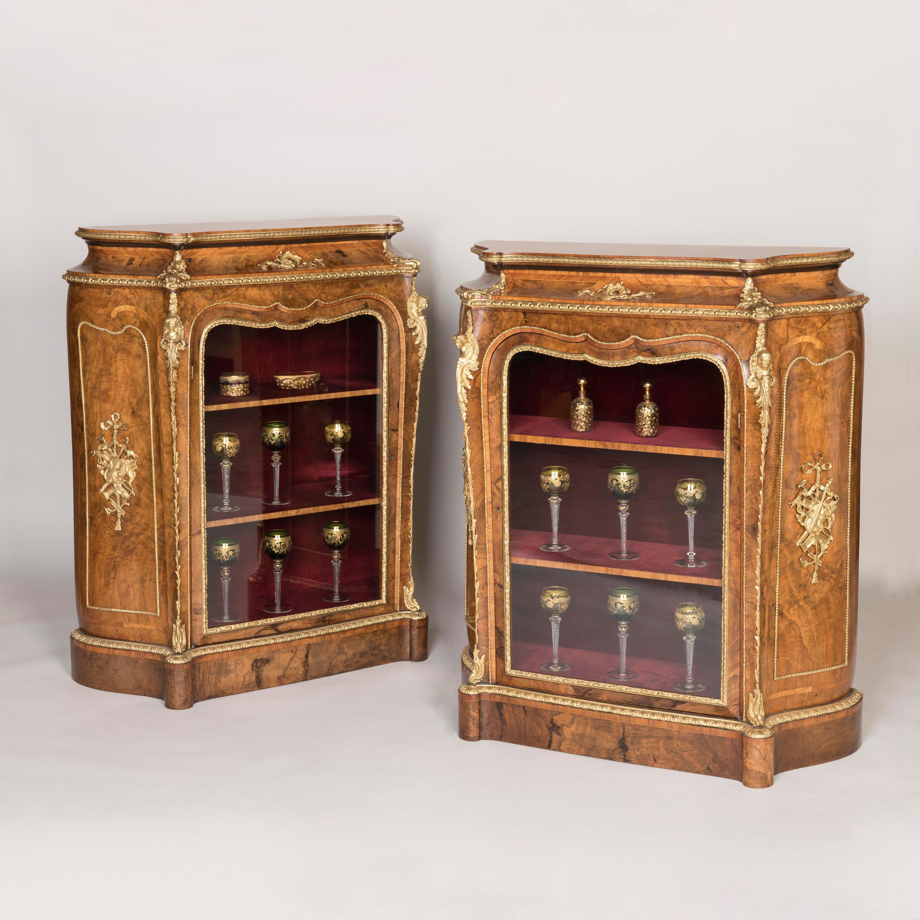 A pair of burr walnut glazed side cabinets.
By Gillows

Designed in the Franglais manner combining English and French features, the side cabinets of serpentine outline veneered in burr walnut with tulipwood crossbanding and gilded bronze mounts,