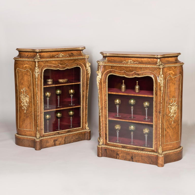 A pair of burr walnut glazed side cabinets.
By Gillows

Designed in the Franglais manner combining English and French features, the side cabinets of serpentine outline veneered in burr walnut with tulipwood crossbanding and gilded bronze mounts,