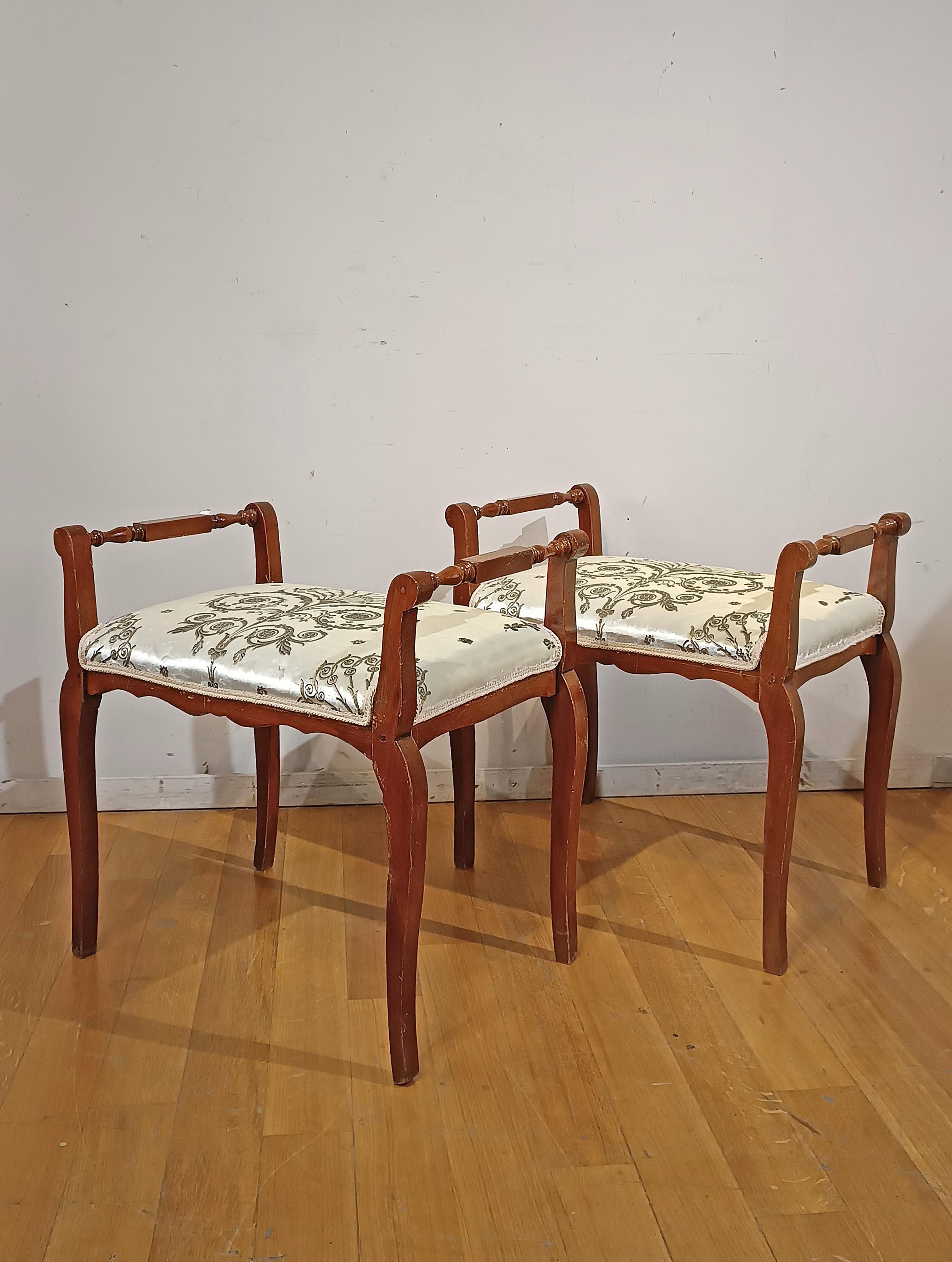 Elegant pair of solid cherry stools, hand-carved. The stools are characterized by turned armrests that give refinement, while the legs have a semi-curved shape. The seat is comfortable, covered with white-silver silk fabric decorated with floral