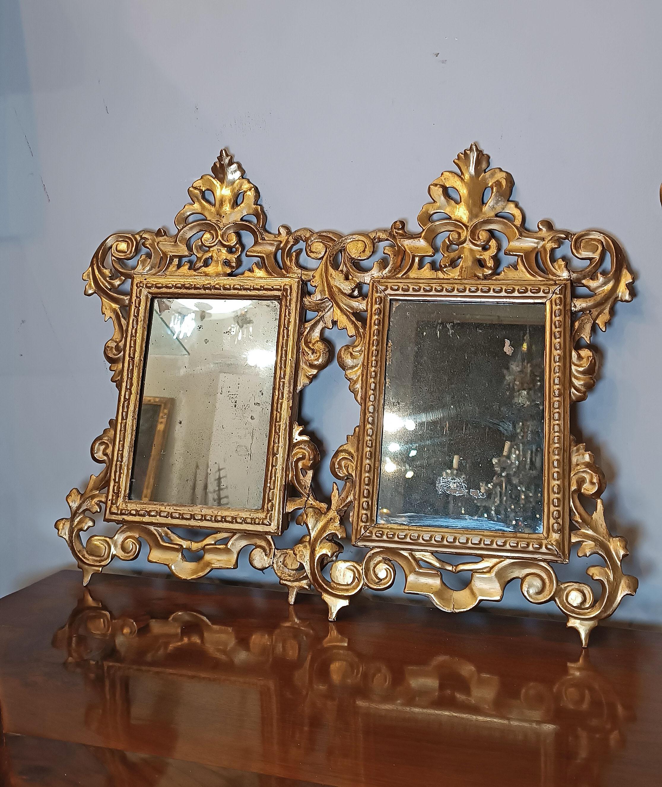 A charming pair of small mirrors in Swiss pine, finely carved and gilded with gold leaf. The frames are adorned with elegant plant spirals that culminate in a cymatium decorated with phytomorphic motifs, as well as the base which is also