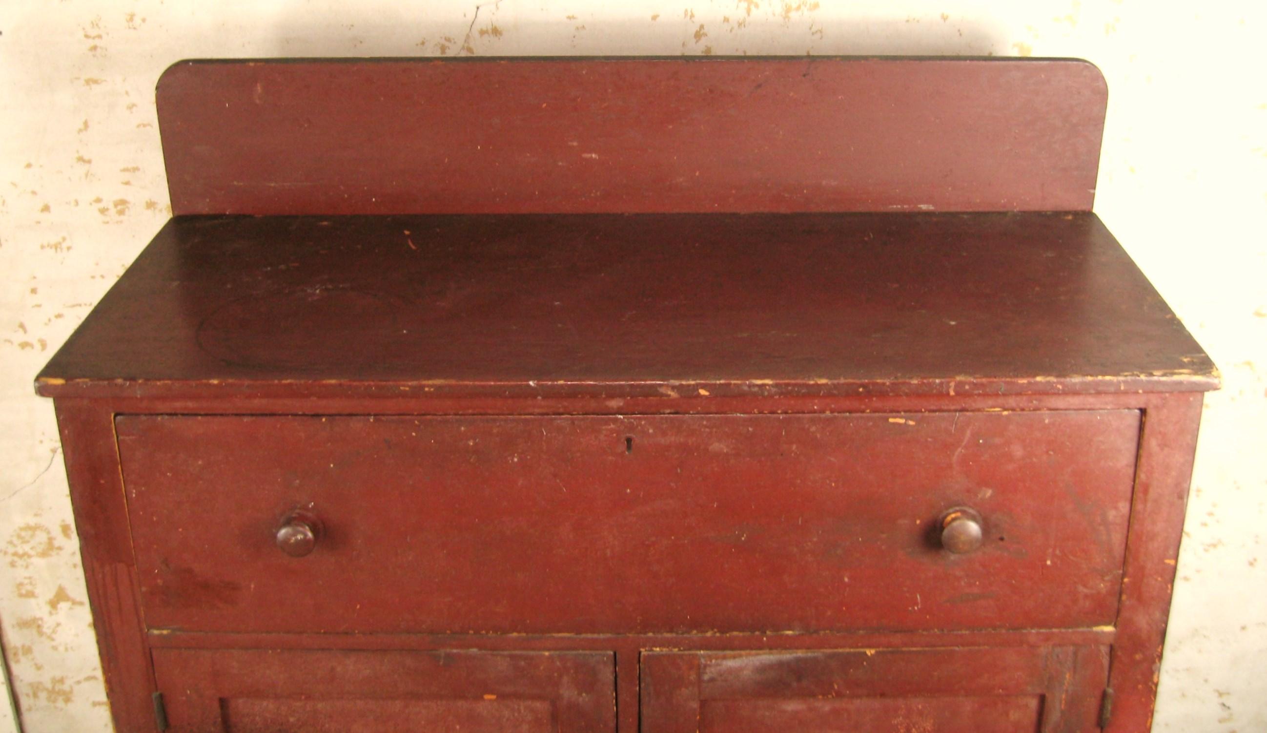 Armoire à confiture primitive du milieu du 19e siècle, peinte en rouge, un tiroir sur deux portes avec une galerie. Il est doté de pieds avant tournés, de charnières et d'étagères. Il a subi quelques réparations au cours de son existence, une porte