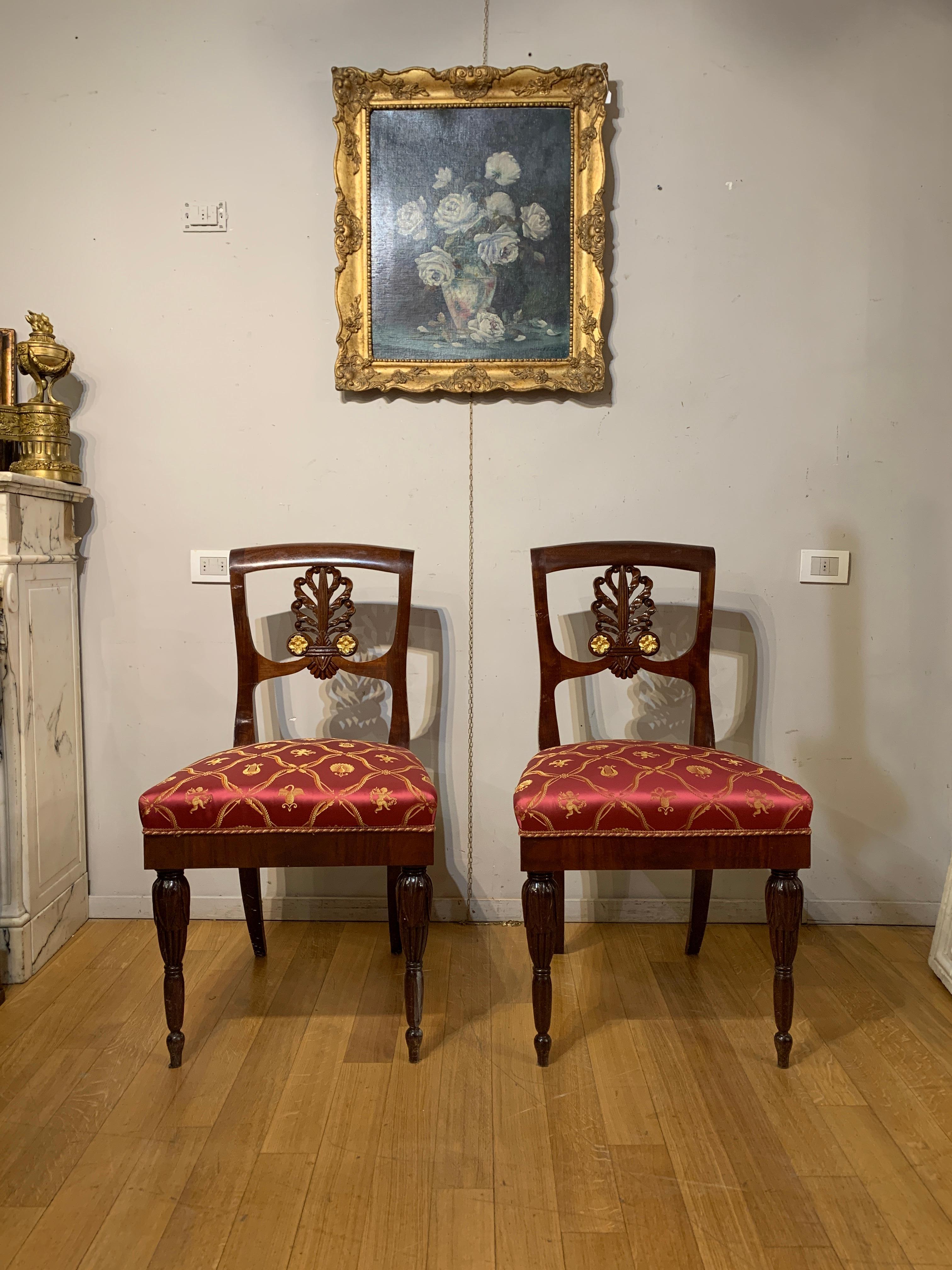 Elegant set of eight Empire style chairs, made of solid carved mahogany, with pure gold finishes. The front legs are shapely and straight, while the rear ones are flared, creating a unique visual balance. The back of the chairs is embellished with a