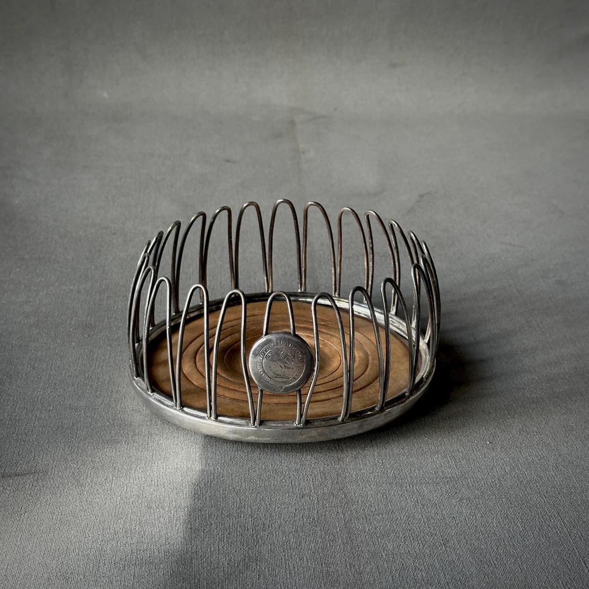 Questo sottobicchiere per champagne in argento di Sheffield della metà del XIX secolo presenta una base in legno splendidamente intagliata e picchetti in filo di ferro elegantemente intrecciati. Il design incorpora un piccolo disco araldico,