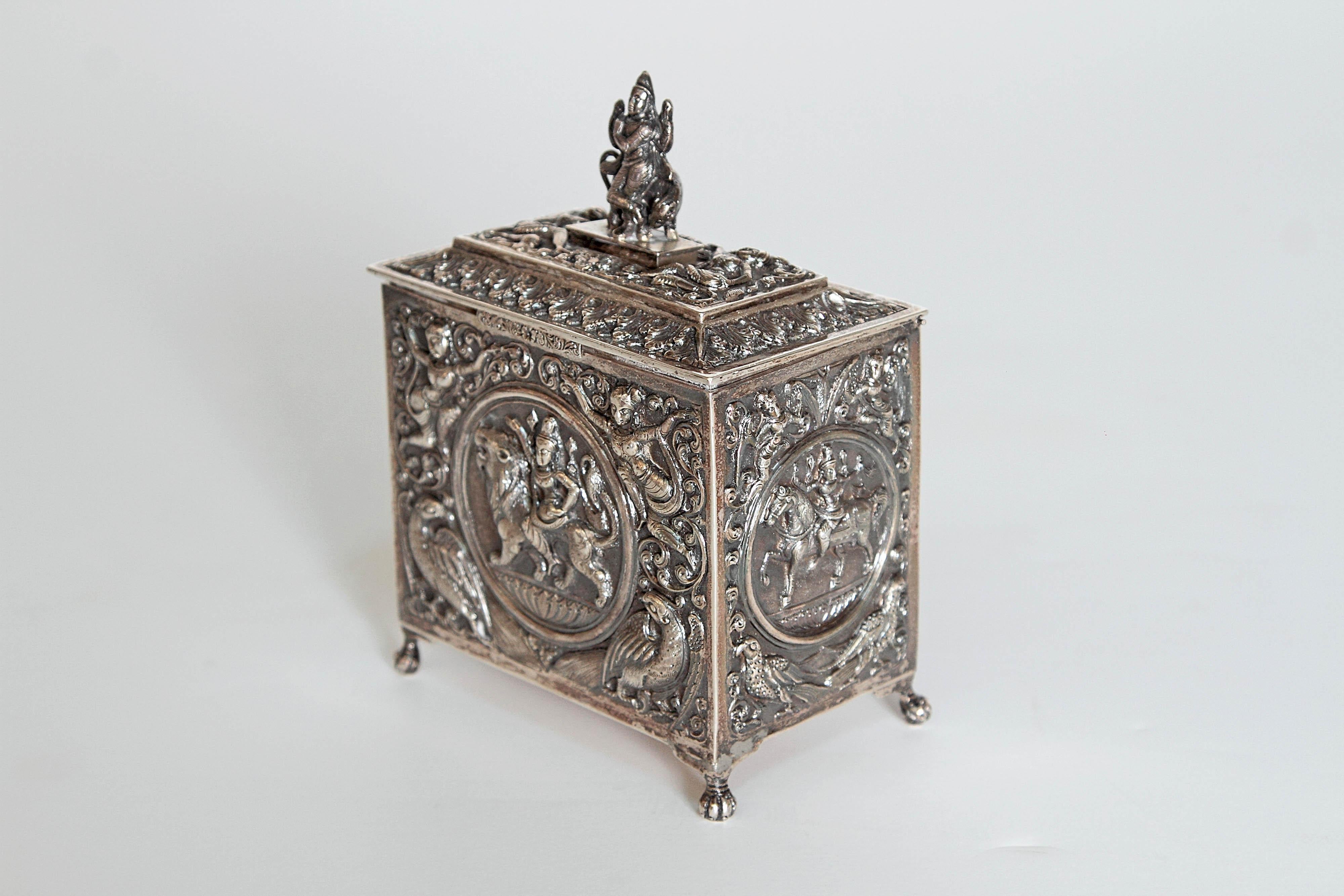 A silver plated small box from Siam. All-over relief with birds, flowers and figures. Woman on lion in front panel and Woman on tiger on rear panel. Woman on horse and sheep on end panels figure on animal as finial on lid, 19th century Siam.