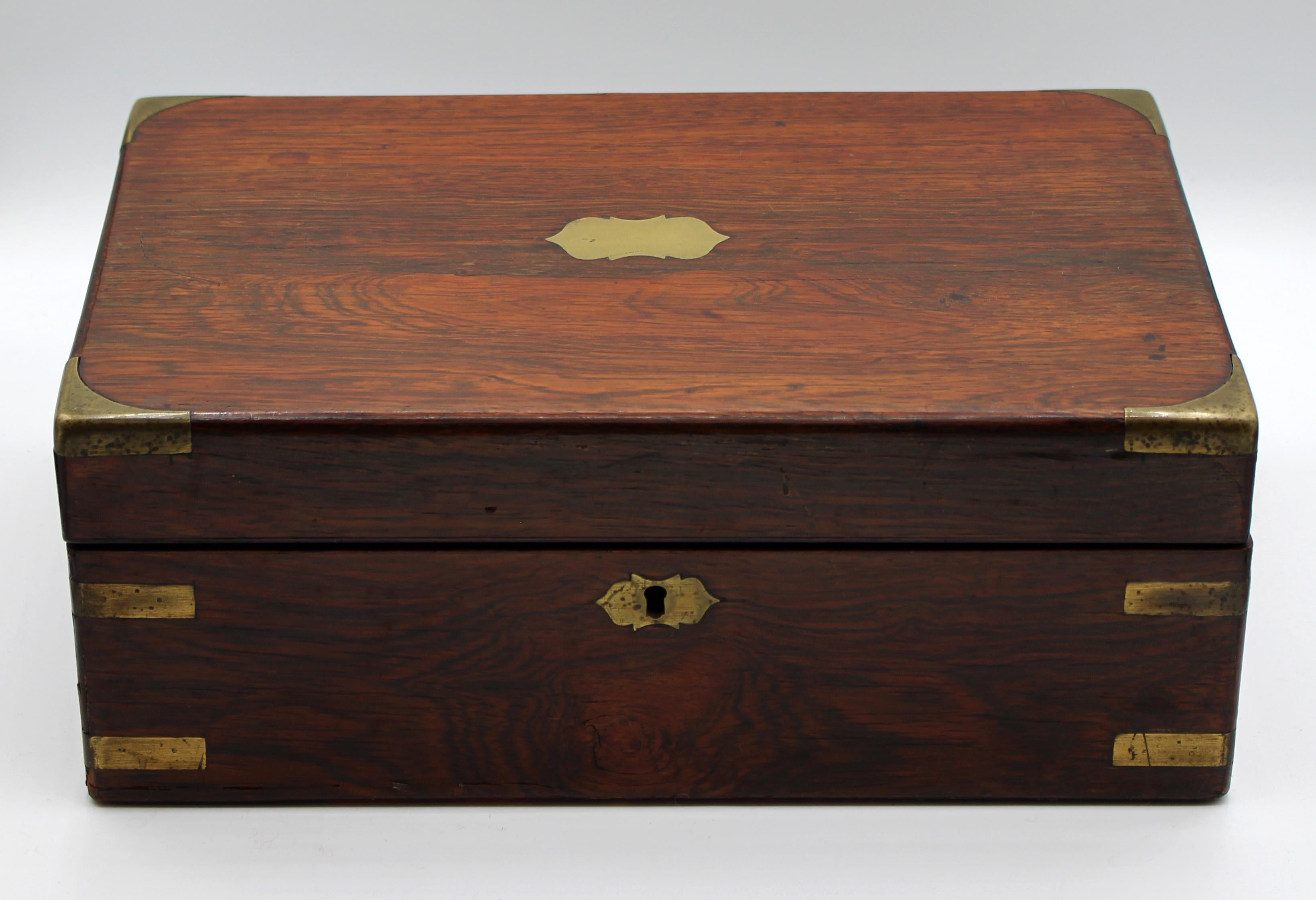 English rosewood lap desk, c.1840-60. Small size. Well mounted in protective brass with brass escutcheons. Fitted interior with two secret drawers. Replaced writing surface. Some veneer losses commensurate with age and use. 13 3/4