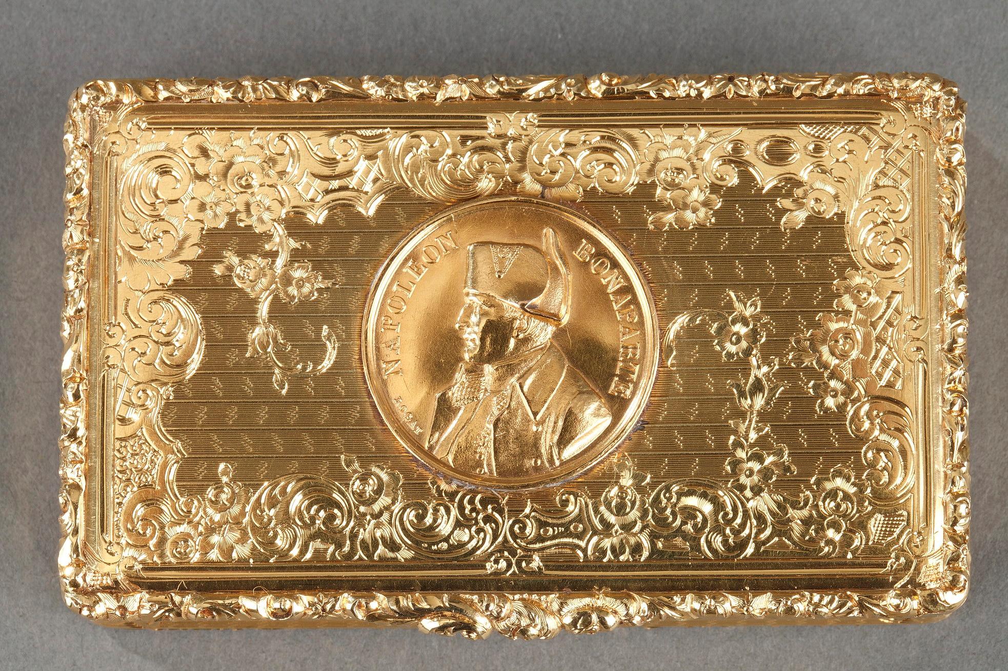 Golddose oder Schnupftabakdose aus ziseliertem Gold mit Blattwerkmuster und Blumenfries. Der aufklappbare Deckel ist mit einem Rogat-Medaillon verziert, das das Profil von Napoleon Bonaparte darstellt: 
