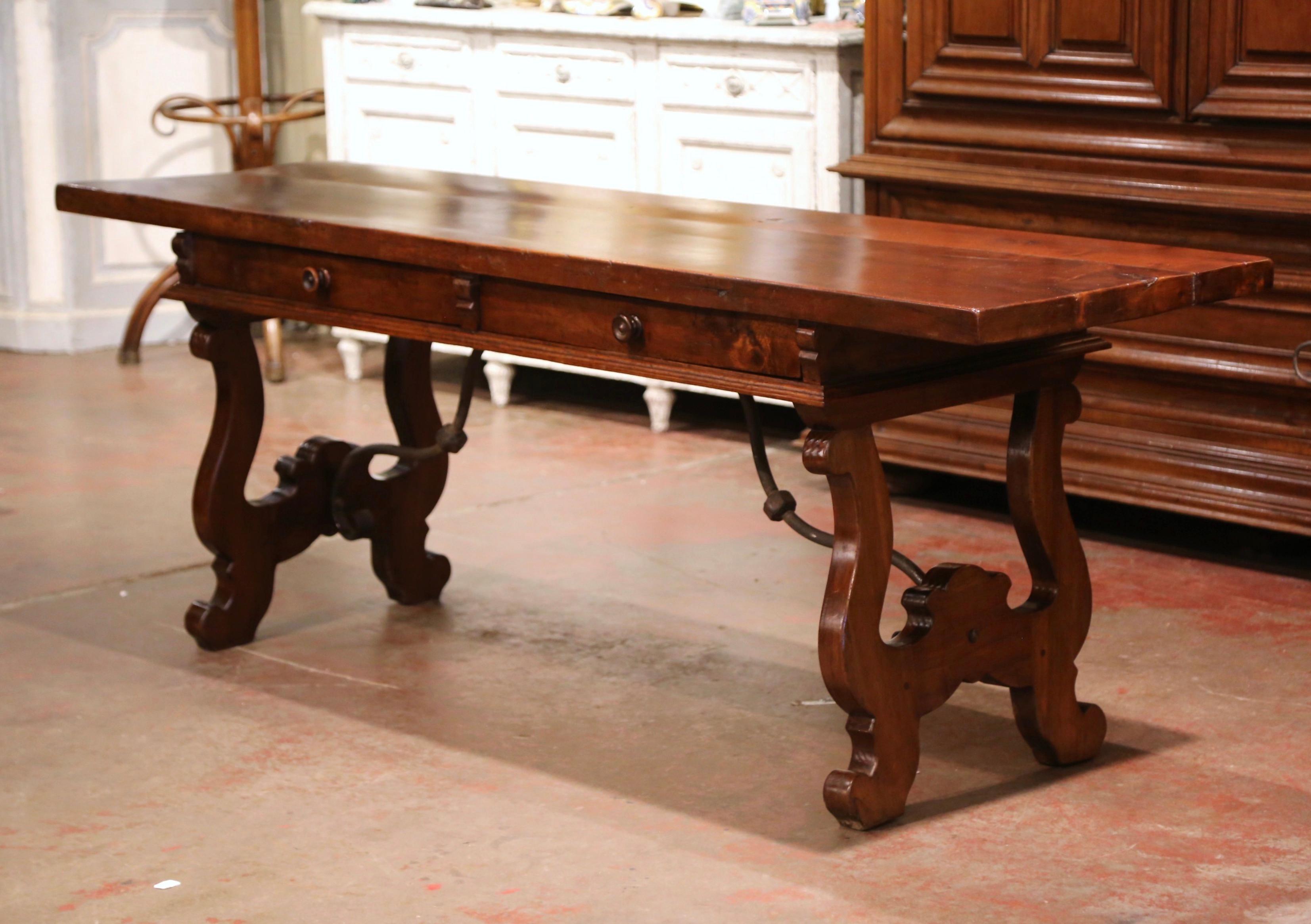 Carved in Spain circa 1870, the long trestle table stands on two intricate carved legs, connected with a thick, forged wrought iron stretcher. The elegant desk features two drawers across the front dressed with the original wooden pulls, over a