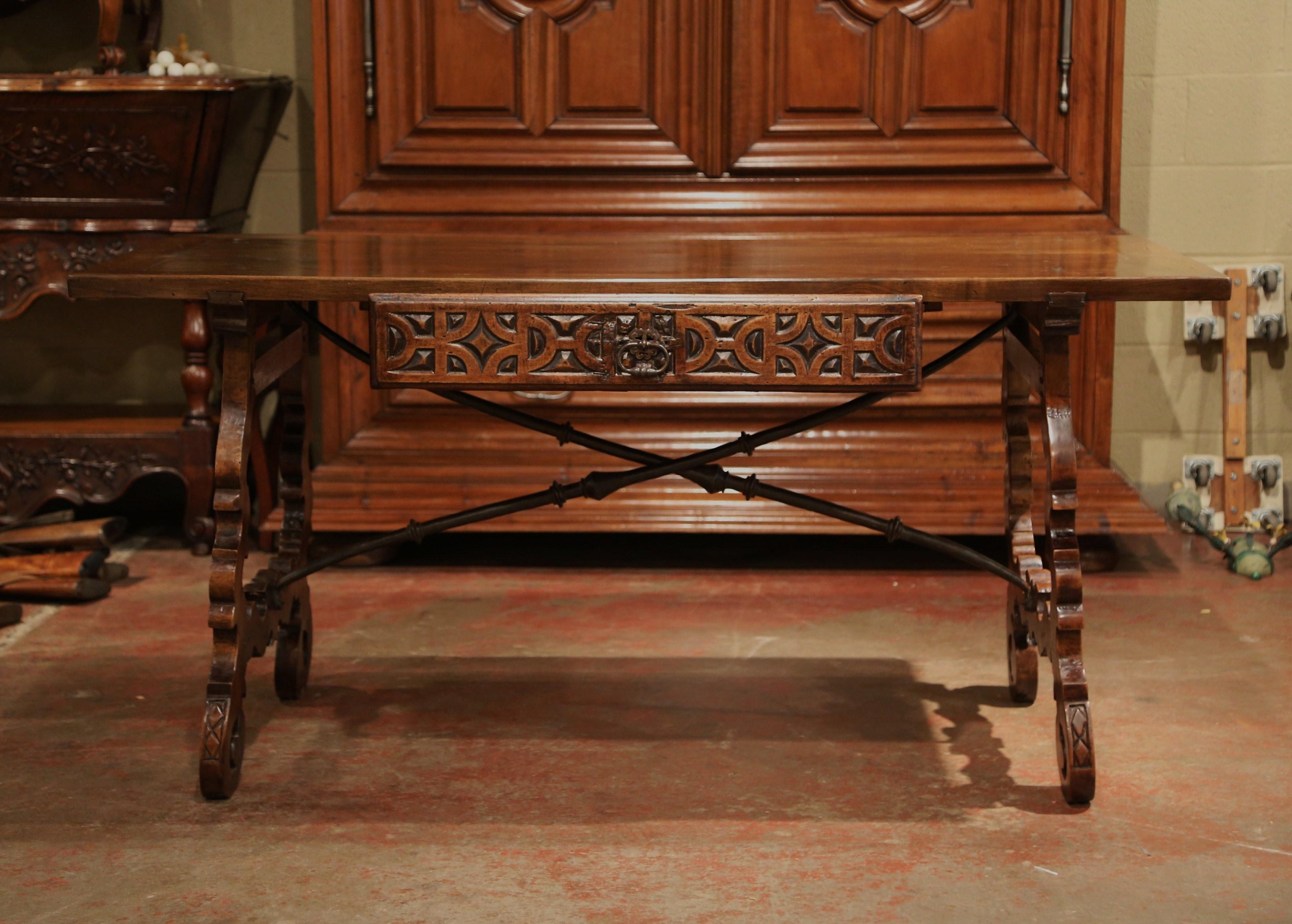Add an elegant focal point to your study or library with this antique Spanish carved fruit wood desk. Carved in Spain circa 1850, the trestle table sits on two intricate legs, which are connected with a thick, forged wrought iron stretcher. The desk