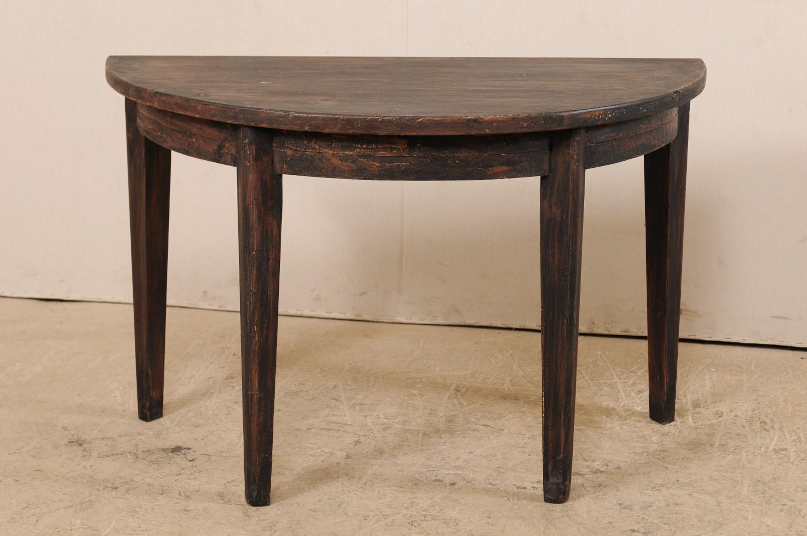 A Swedish demilune table from the mid-19th century. This antique demilune table from Sweden features a half moon top over rounded apron, all raised upon four squared legs which taper gently at their feet. There is a dark finish with ebony, which