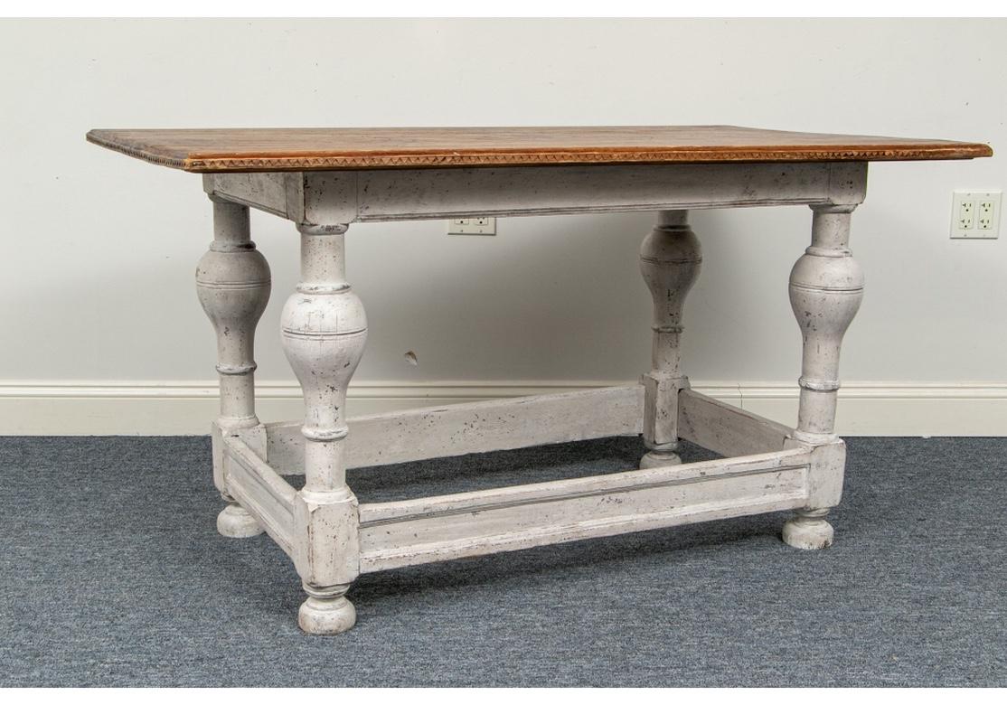 A rectangular table with a pine plank top with carved edge and decorated with incised flowering vines. Mounted on a base in white paint with baluster turned legs, flat stretchers all around and bun feet.
Measures: Length 56 1/4