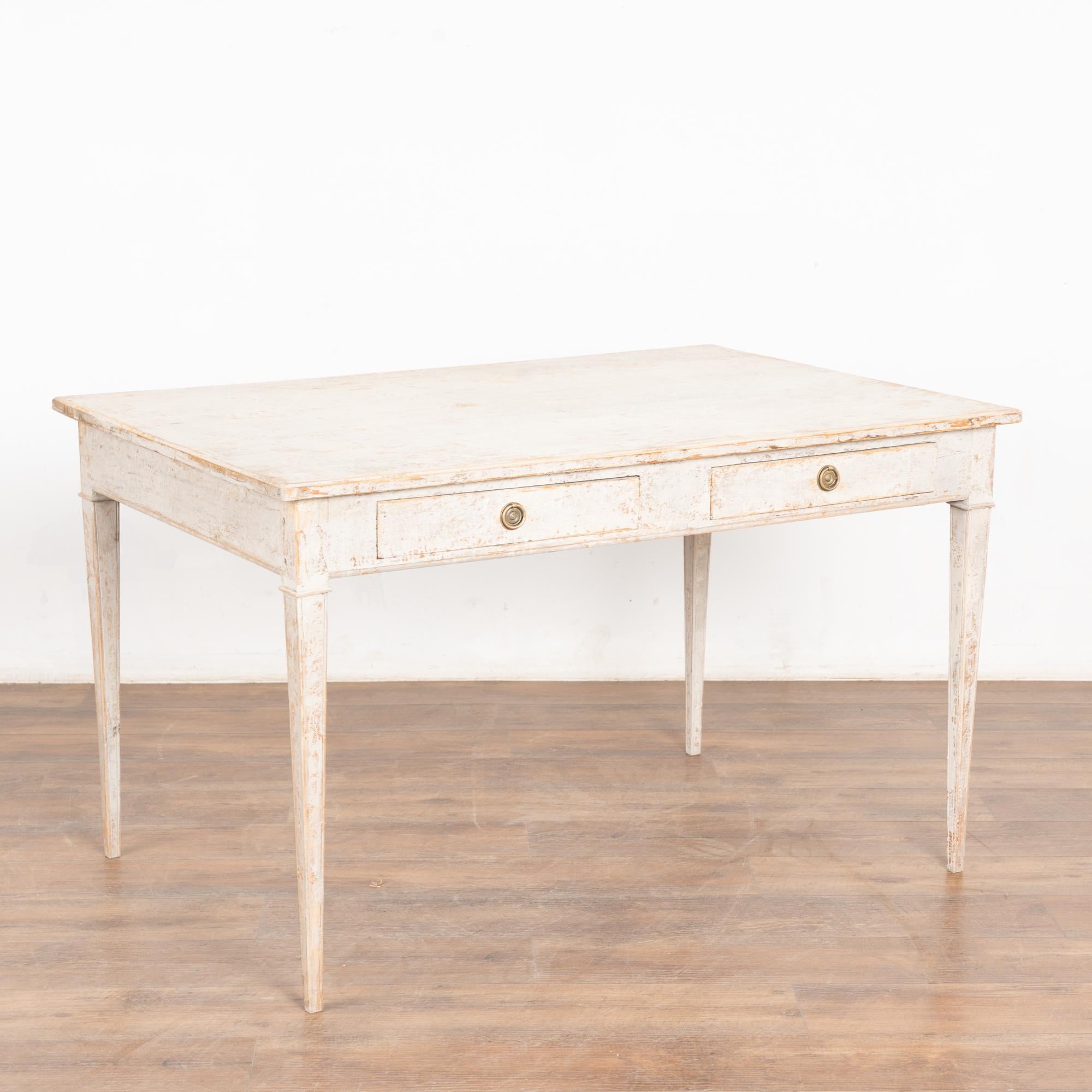 Ancien bureau d'associé en pin peint en gris, de style suédois gustavien, avec deux tiroirs de chaque côté de la table et des pieds cannelés effilés traditionnels.
La finition peinte présente des couches de gris clair et de blanc antique, avec