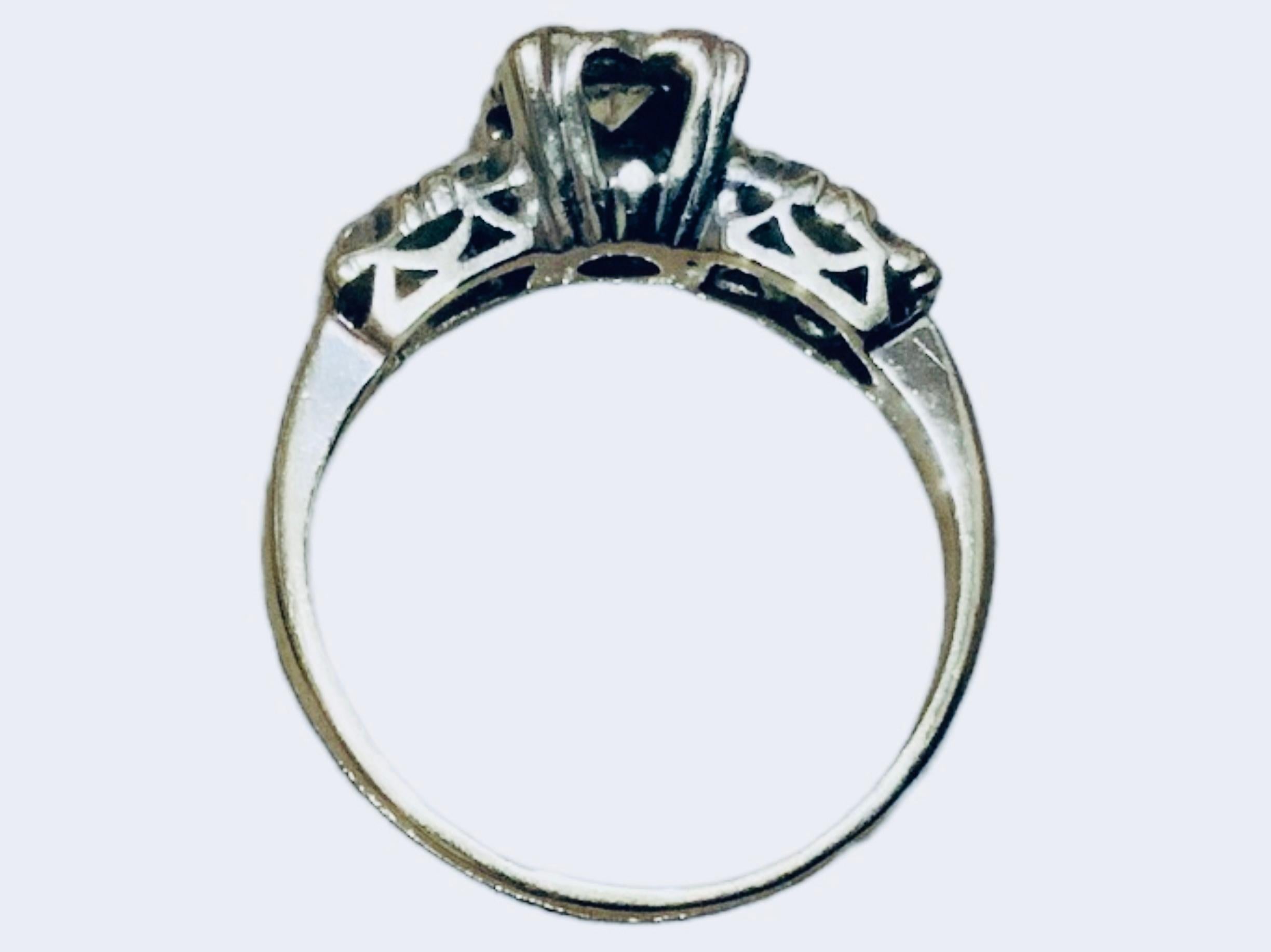 This is a 14 K White Gold and Diamond Wedding Ring. It depicts a white gold band adorned with four small flowers in a row and a large one in the center. All of them enhanced by a single cut diamonds, being the center one a round brilliant cut. It is