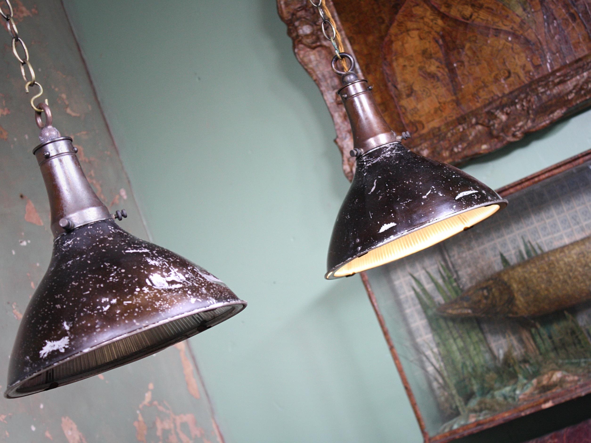An original pair of Holophane industrial pendants, with original well worn factory scumble paintm, mid-20th century.

The pressed aluminium casing, houses a prismatic glass Holophane shade finished with a bronze gallery and hanging hoop. 

Well