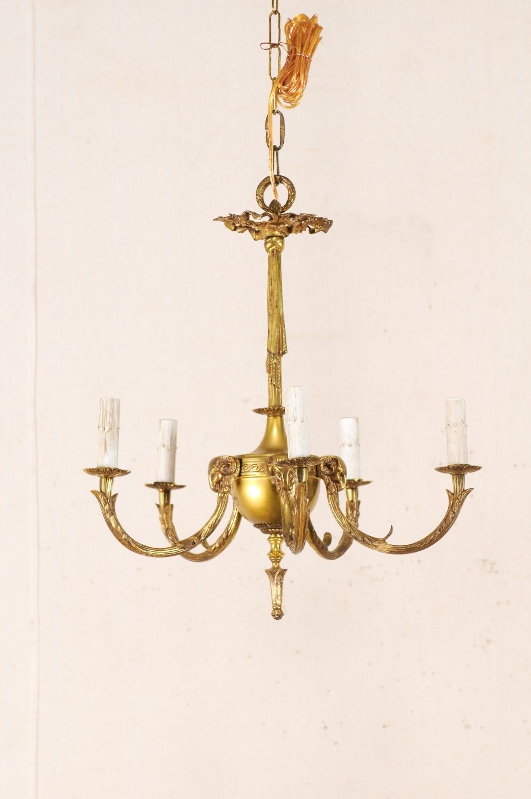 A French brass five-light chandelier from the mid-20th century. This vintage hanging light from France is adorned with rich foliage accents and ram's head motif. Five rams's heads top the light arms which extend outward in a C-shaped swag, each