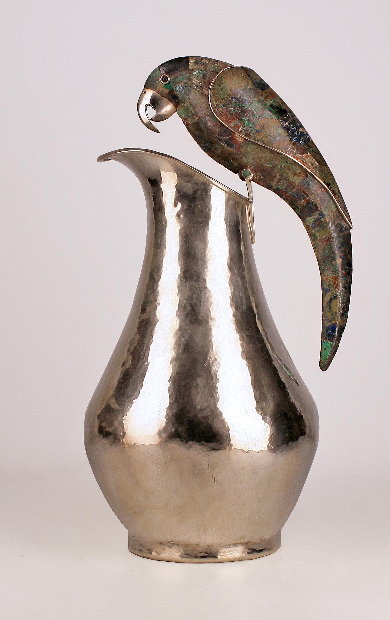 Mid-20th century mexican hand-crafted silver pitcher with crushed gemstone inlay parrot handle by Los Castillo

By: Los Castillo
Material: abalone, copper, lapis lazuli, malachite, silver, silver plate, stone
Technique: cast, hammered, hand-crafted,