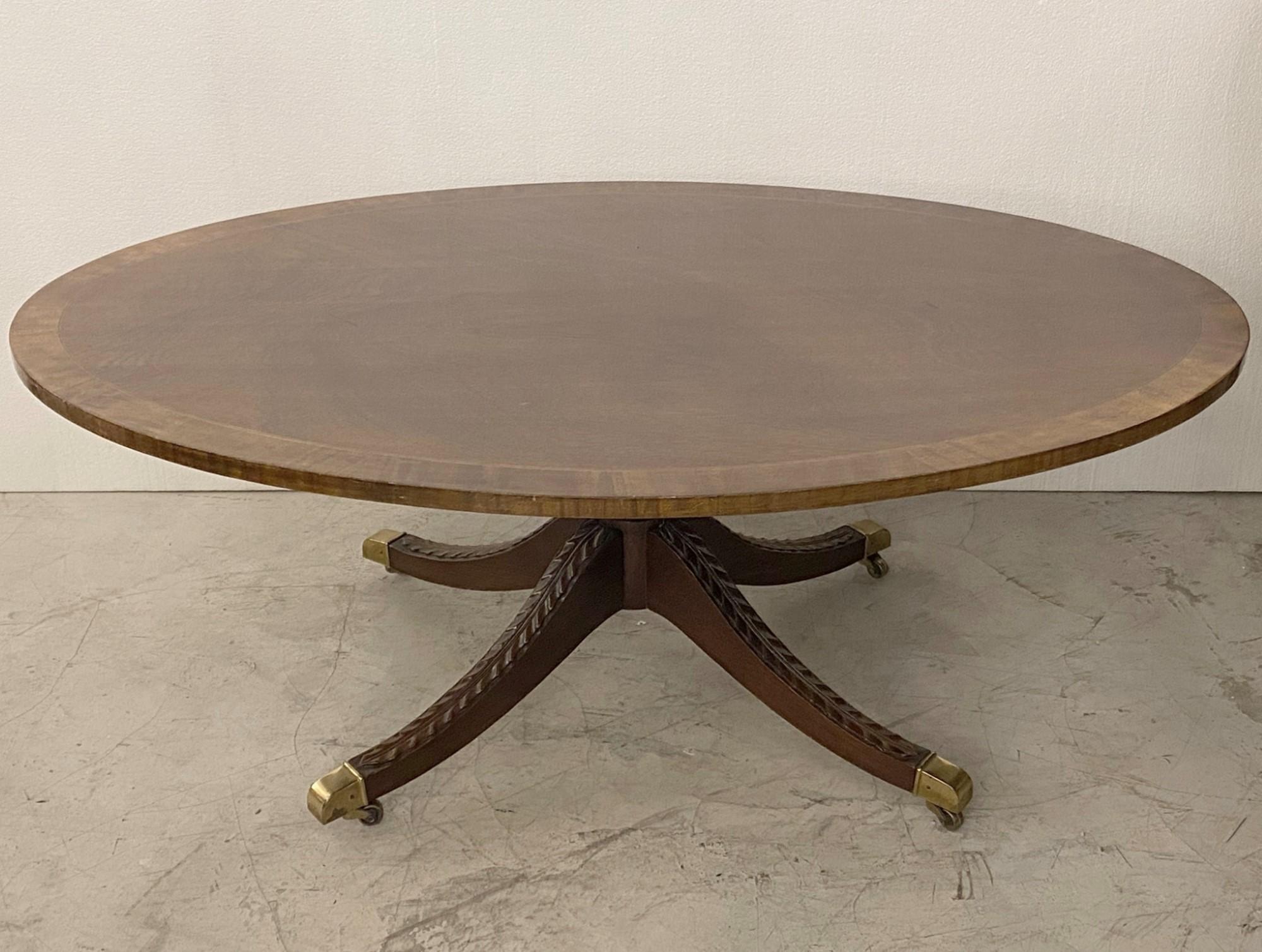 Mid-20th century oval walnut coffee table with inlays. Features floral carving on gently curved legs that are finished with wheeled brass claw feet. Made by Kindel Furniture out of Grand Rapids, MI. This can be seen at our 2420 Broadway location on