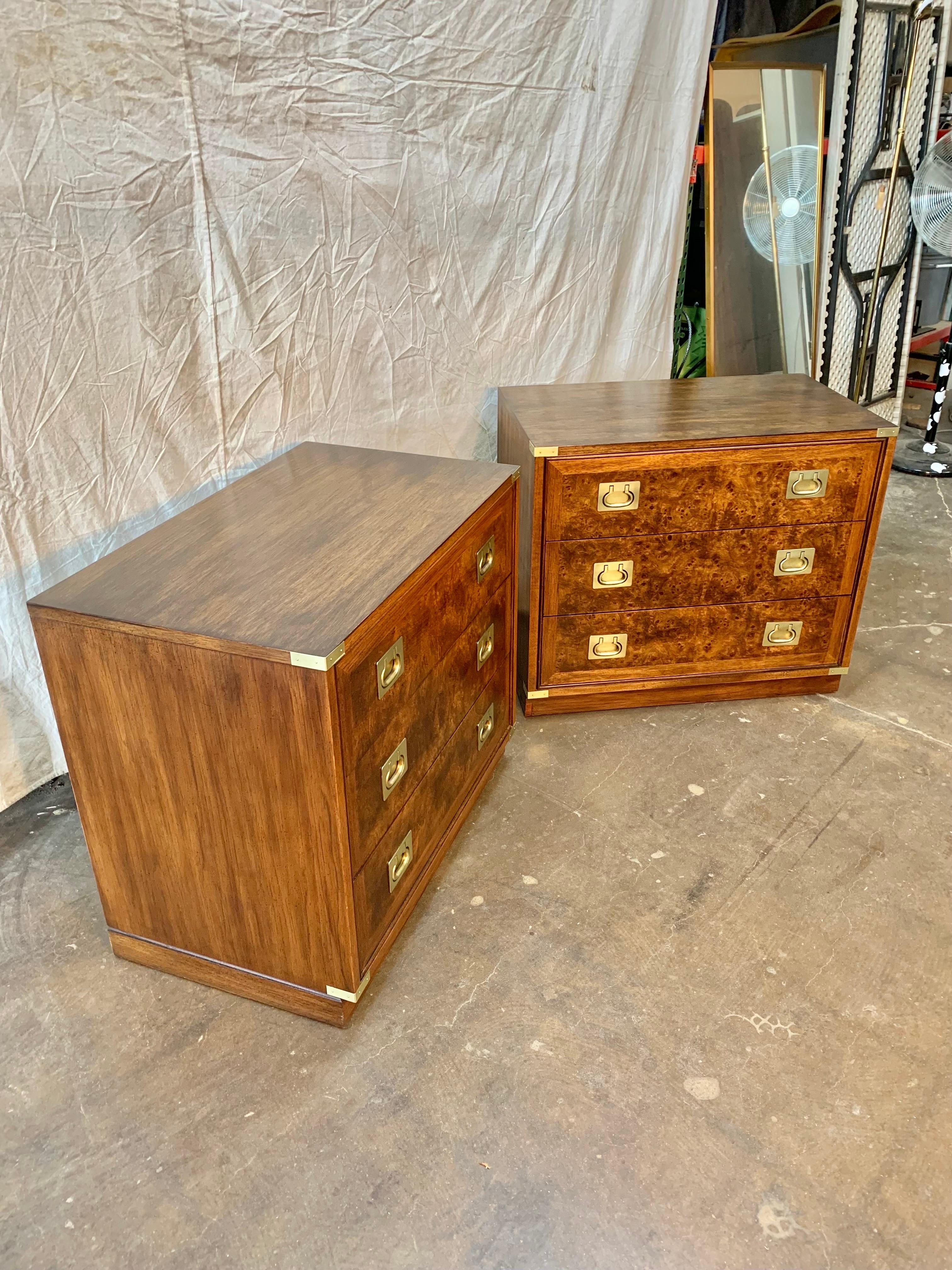 This pair of Campaign Style Bachelor Chest of Drawers were manufactured in the Mid 20th Century by the Hickory Manufacturing Co. Each chest is constructed of solid heavy walnut with Burlwood Venner on the front of each drawer. Both pieces feature