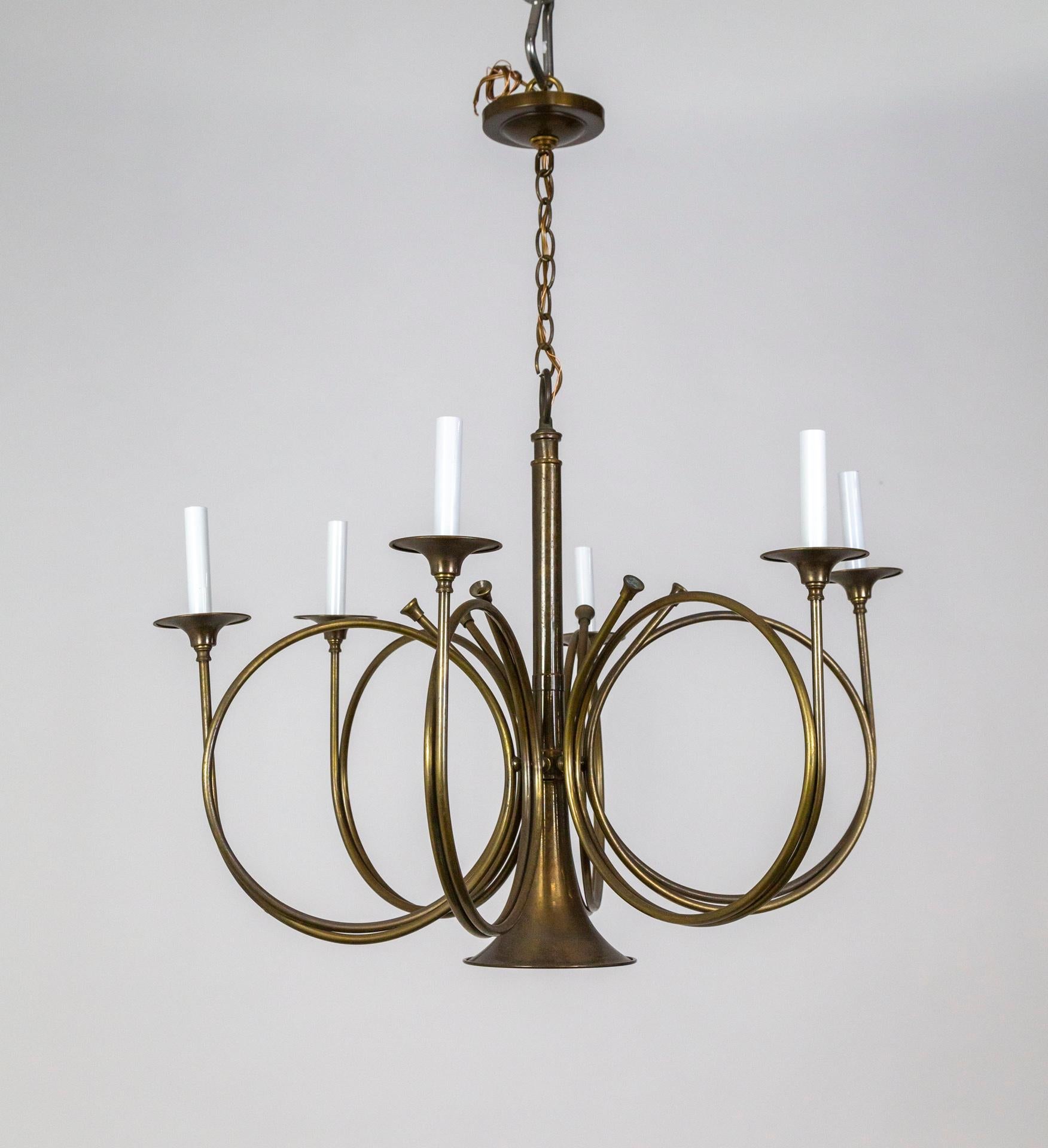 A patinated brass chandelier comprised of French hunting horns designed by Fredrick Cooper. Six arms curl out from the central horn form with up-lights, candlestick style, and the openings of the horns act as bobeches. There is one hidden downlight