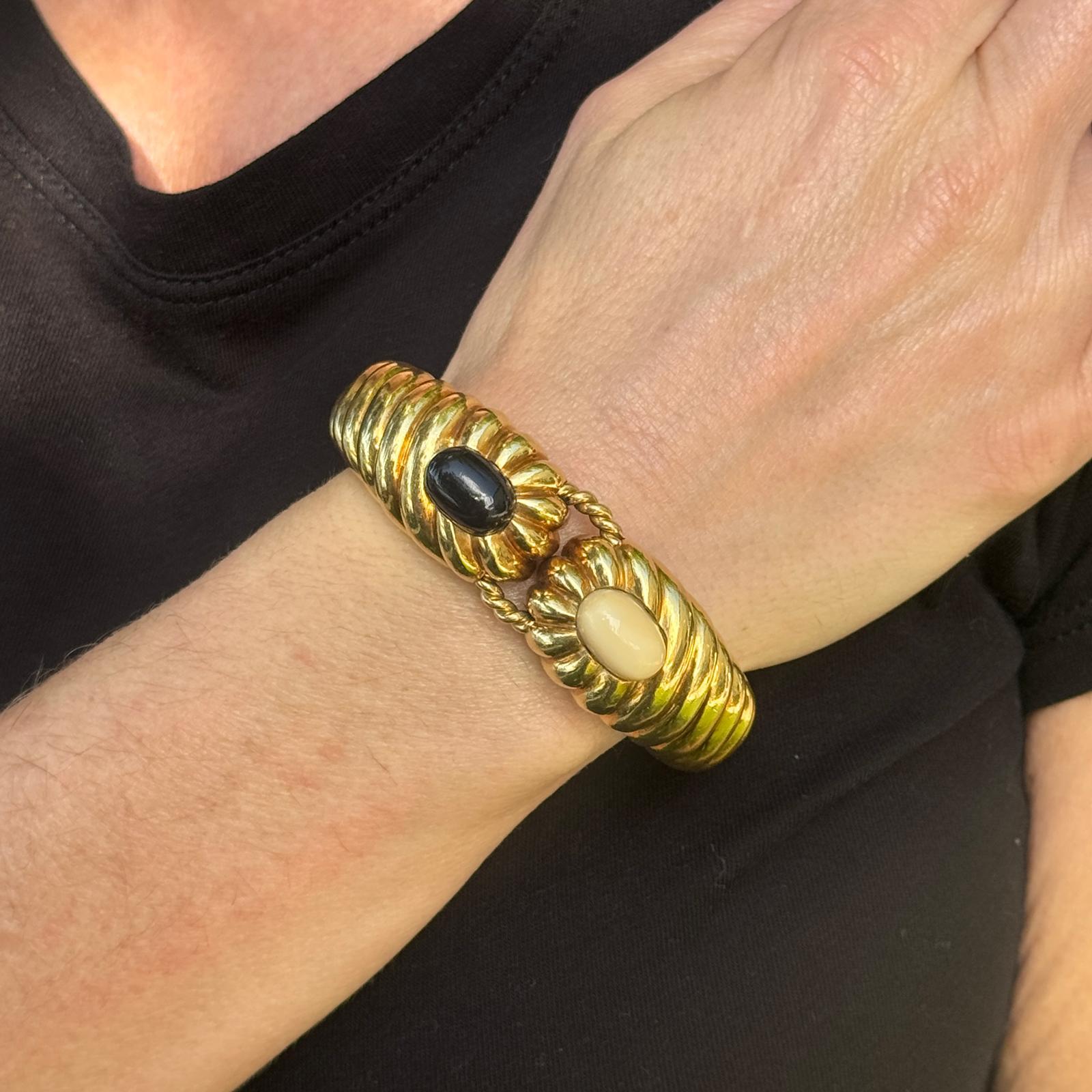 This elegant mid-20th century 18k yellow gold ribbed hinged bangle is a stunning example of timeless sophistication. The bracelet features a sleek ribbed design that gradually tapers in width from 0.5 to 0.75 inches, adding a dynamic touch to its