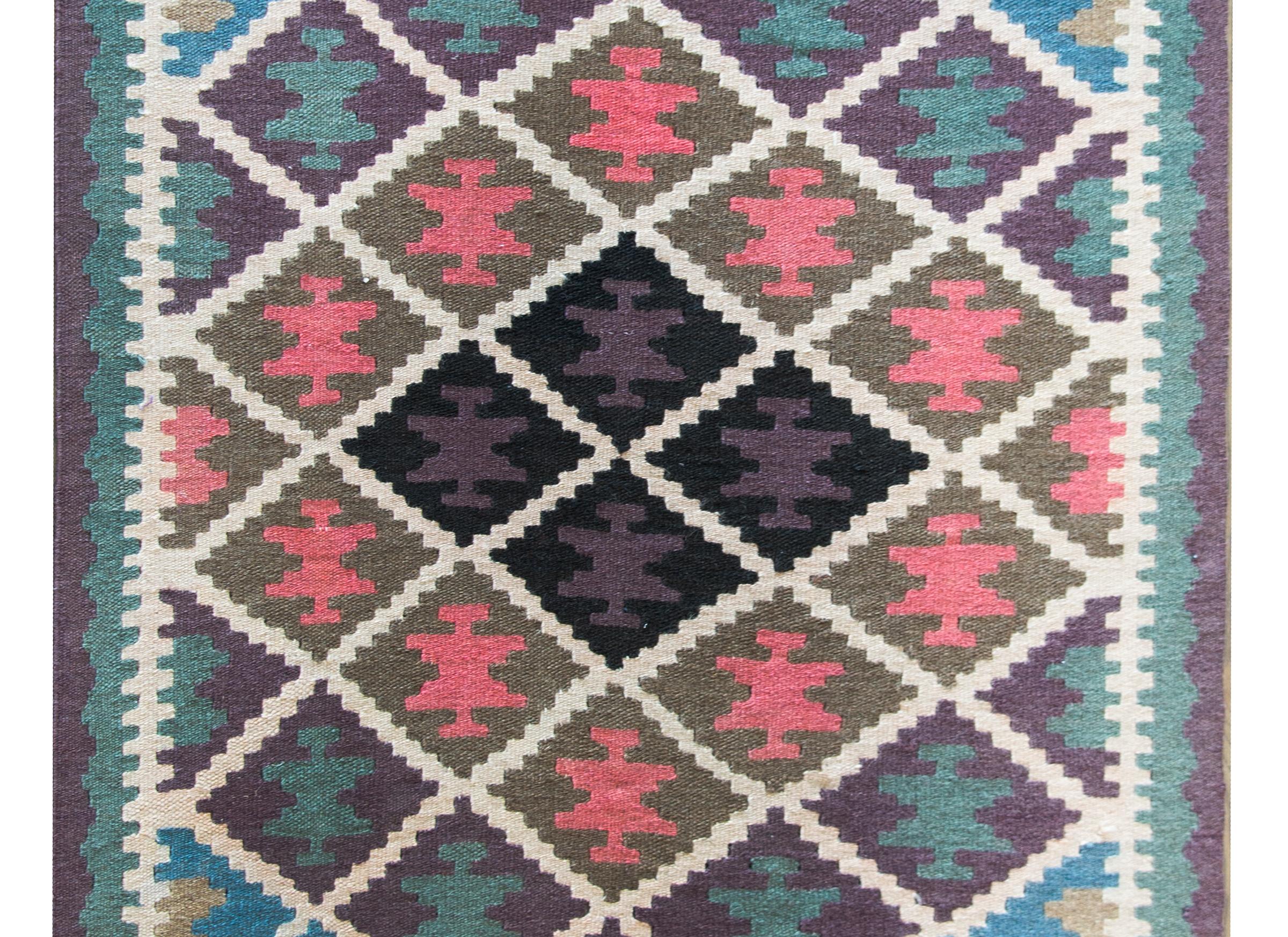 A wonderful mid-20th century Afghani kilim rug with an all-over diamond pattern, each with a stylized flower, and woven in brilliant pinks, indigos, golds, teals, and violets.