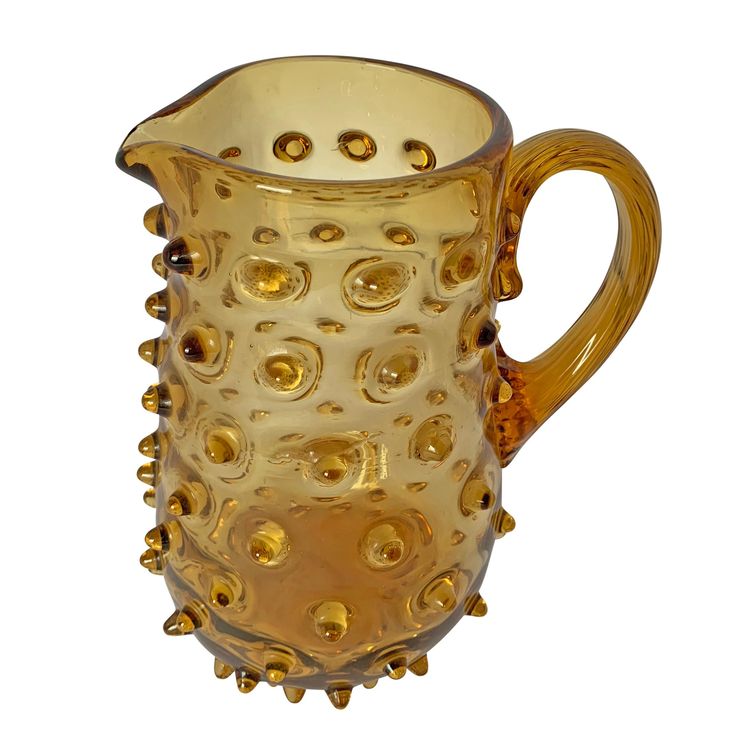 A fanciful early 20th century American amber glass pitcher covered in spiky hobnails with a pulled and applied handle. This pitcher also makes a beautiful flower vase.