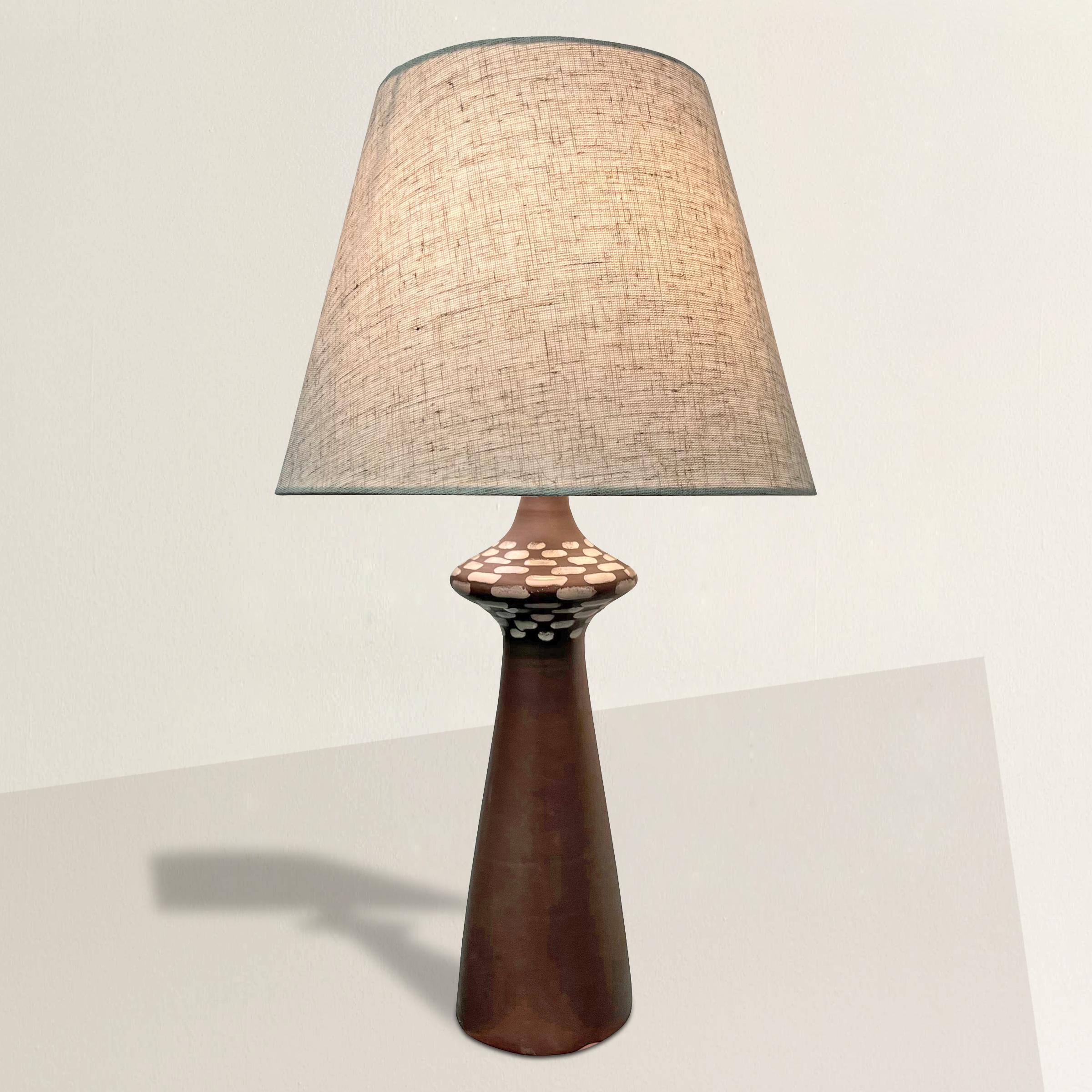 Cette lampe à poser américaine en céramique du milieu du XXe siècle incarne le mélange parfait entre charme vintage et fonctionnalité moderne. La lampe présente une étonnante glaçure brune mate, élégamment contrastée par un motif géométrique blanc
