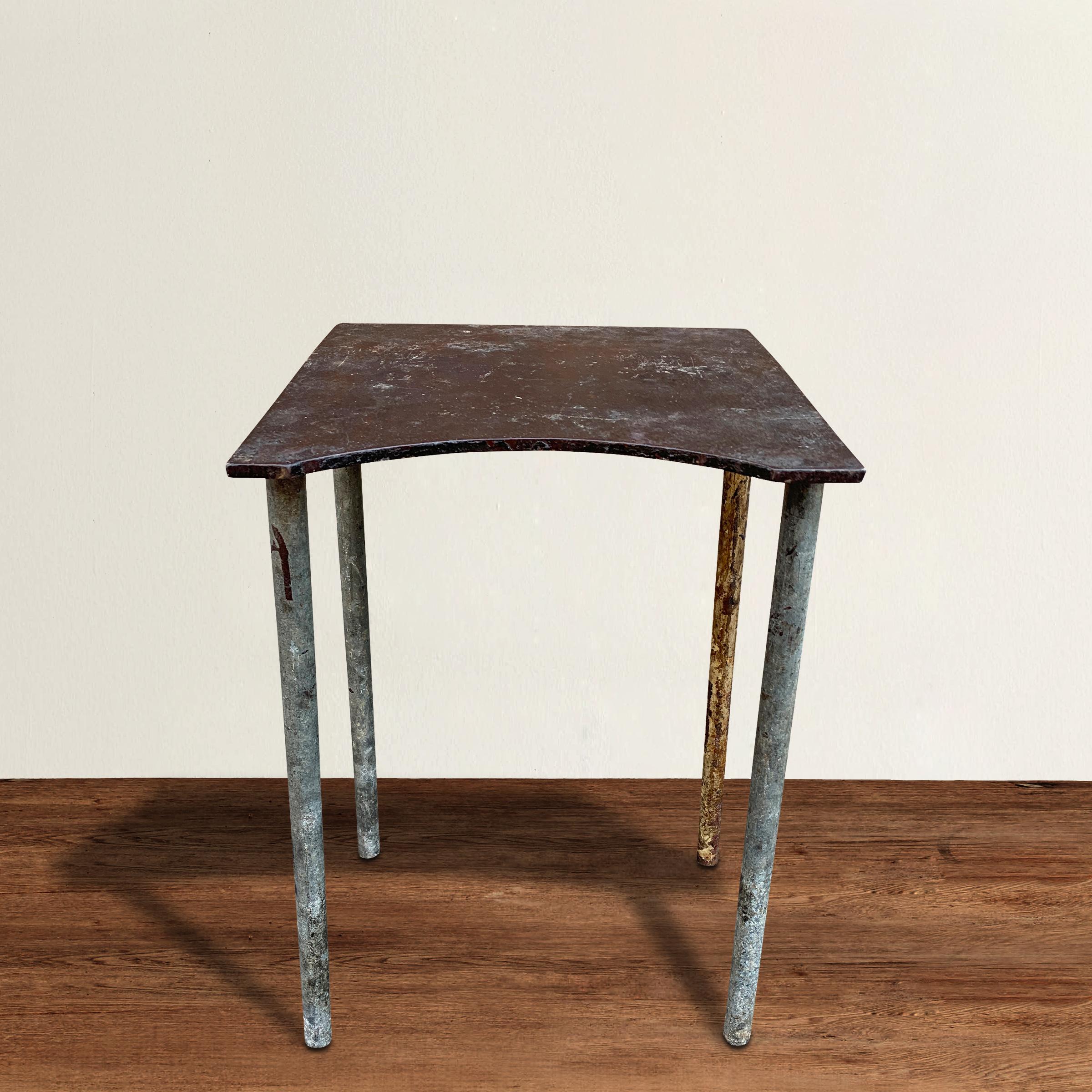 An honest and stoic mid-20th century American industrial steel table or stool with a put form including round legs supporting a mostly square top with one side having a half moon cut out. Works wonderfully as a drinks table next to your favorite