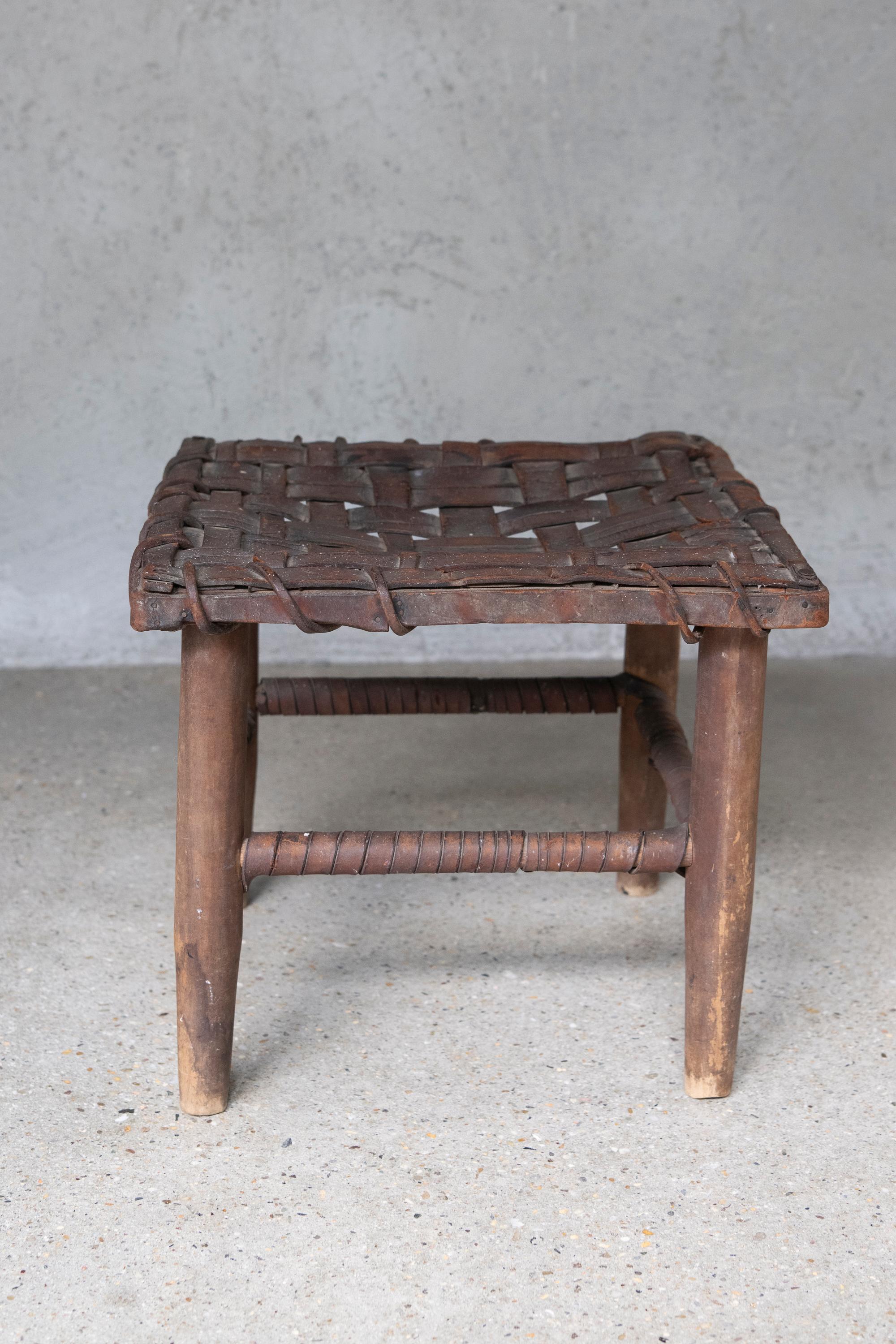 American rustic stool with a handwoven leather strap seat over a wood frame. Constructed with turned legs and stretchers,  reinforced by additional leather wrapping.
----
A finely proportioned American handcrafted stool from the mid-20th century,