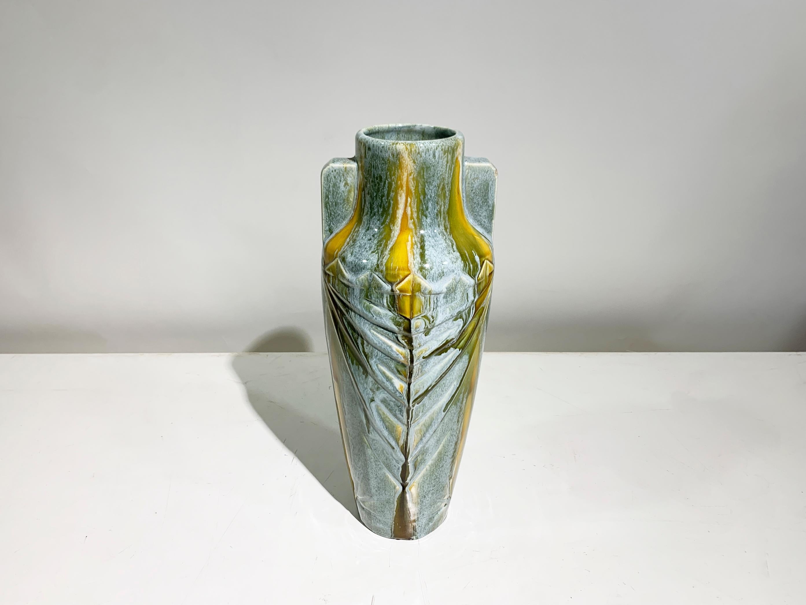 La forma ad anfora del vaso, caratterizzata da un collo stretto e un corpo più largo, è esaltata dalla precisione geometrica del design. Presenta due sottili maniglie allineate verticalmente, integrate perfettamente nel corpo, che conferiscono
