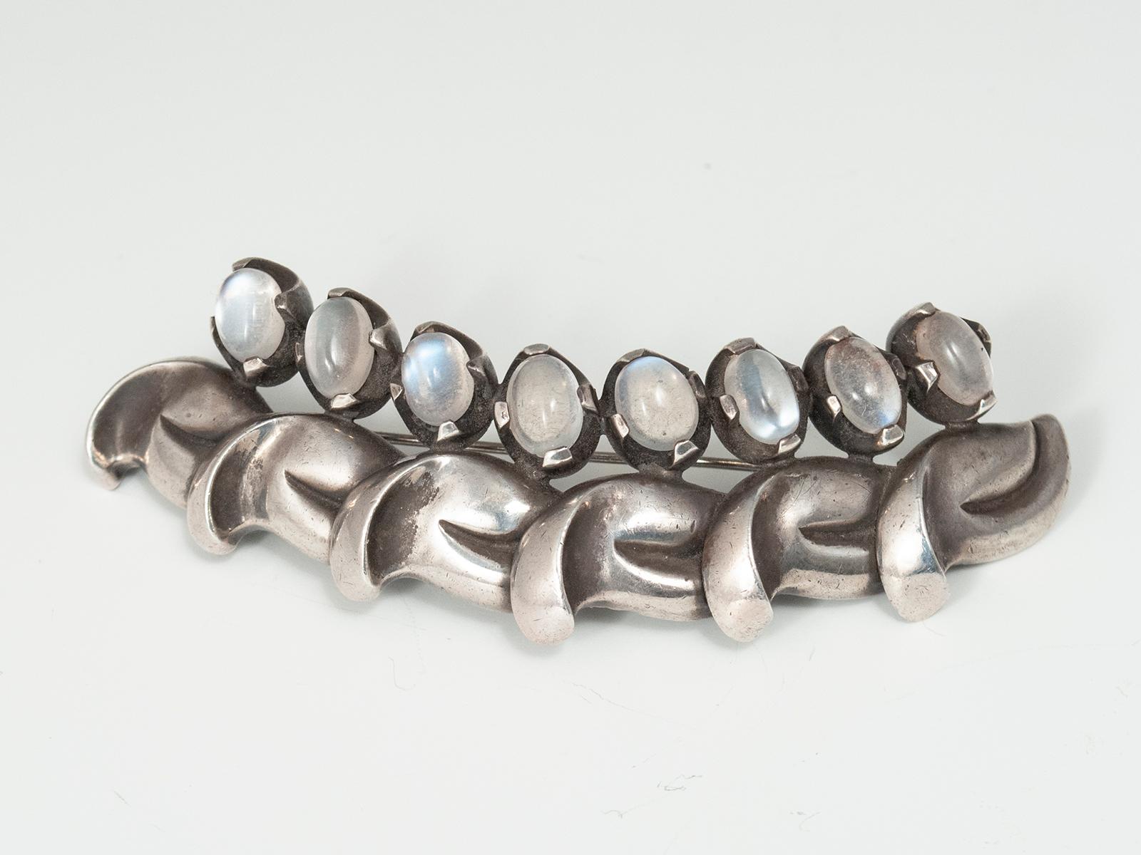 Mid-20th Century Antoñio Pineda (1919-2009) Silver and Moonstone Brooch, Taxco, Mexico

This beautifully crafted silver brooch contains eight oval-cut moonstone cabochons set in a curved row above six stylized leaves. The marks on the back of the