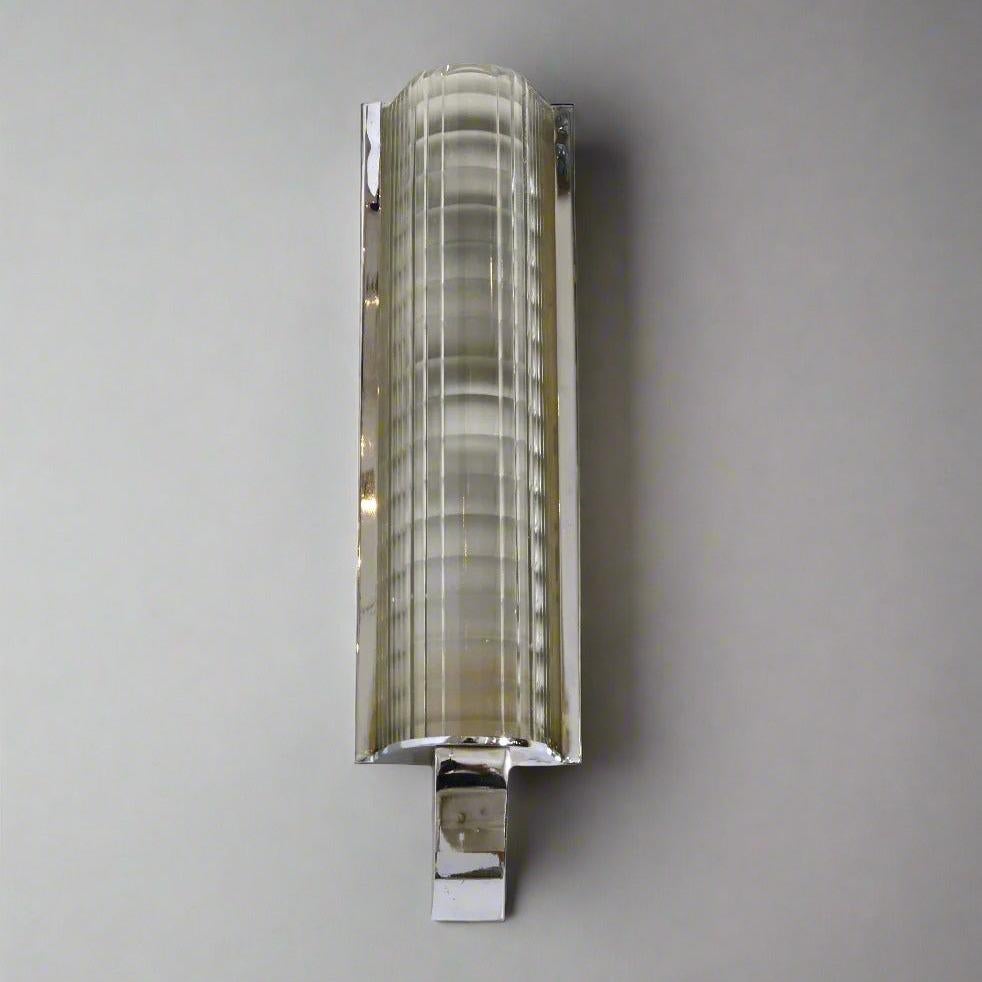Une seule applique murale d'époque Art Deco en chrome poli et verre nervuré moulé. Le design se caractérise par une haute forme verticale en verre qui repose sur une base chromée en quart de rond.  Cette fixation murale est suspendue verticalement