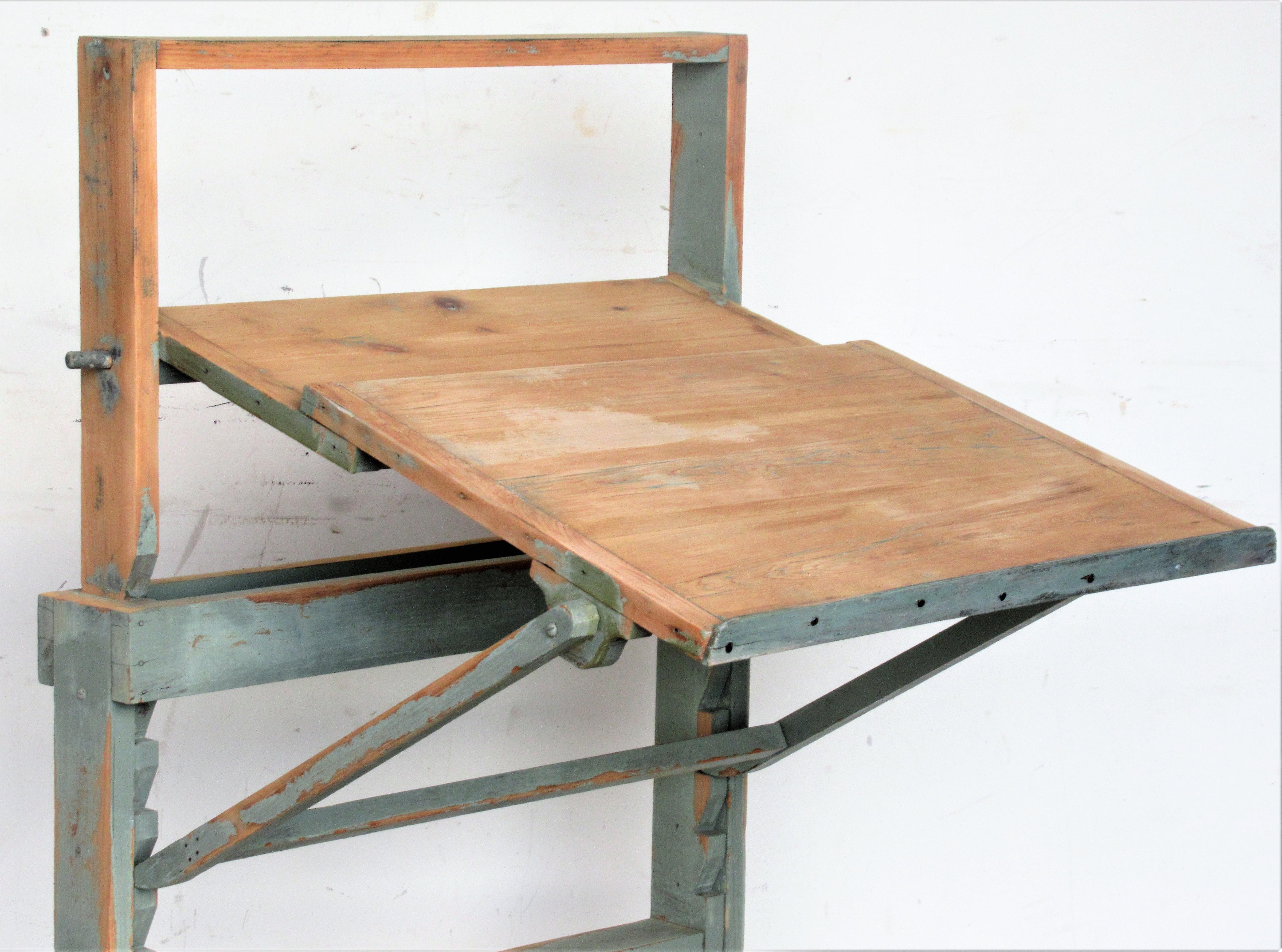 Adjustable height pine drawing drafting table desk in nicely aged old pale sea foam green painted and partially stripped surface. There are five notches on each side of framework that the wood rods will sit for raising and lowering the height and