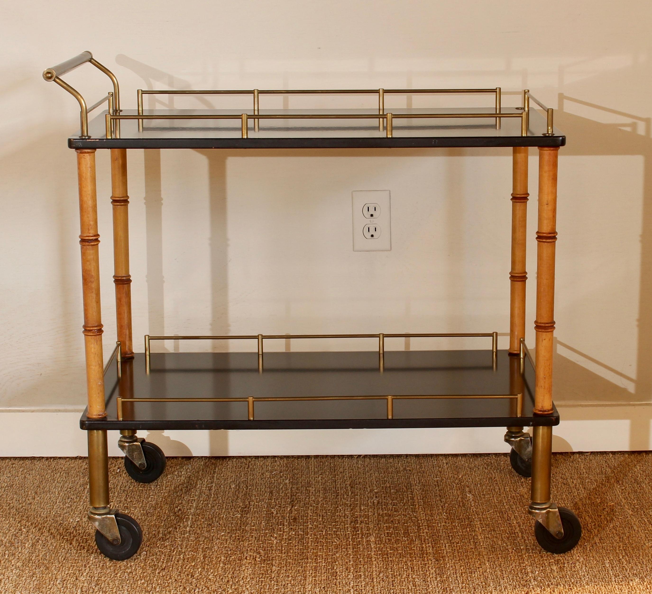 A brass and ebony Hollywood Regency two-tier bar cart on turned wood faux bamboo legs terminating in sturdy rubber wheels.